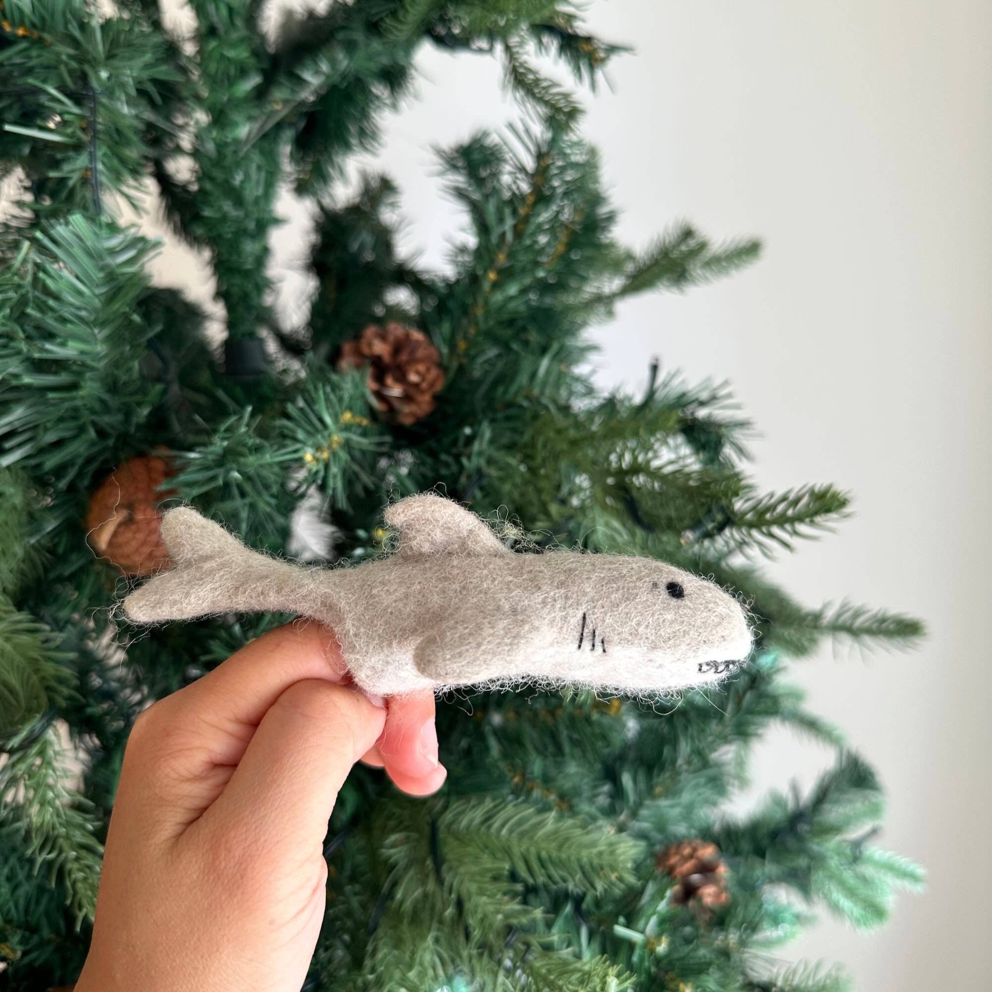 Hand holding a shark-shaped toy in front of a decorated Christmas tree