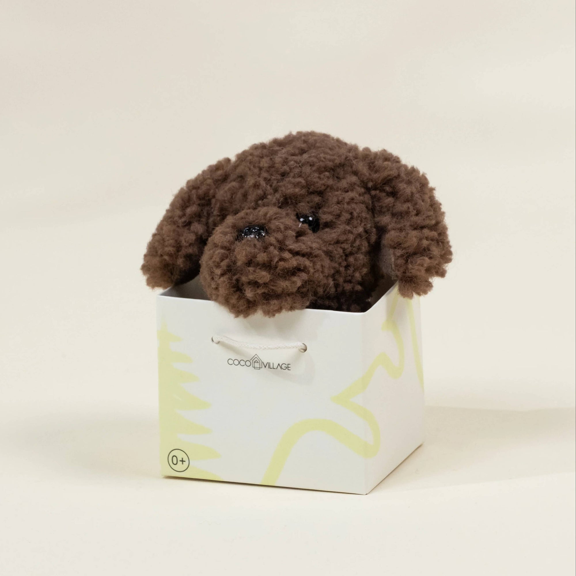 Brown plush toy dog in a white box with a brand logo on a beige background