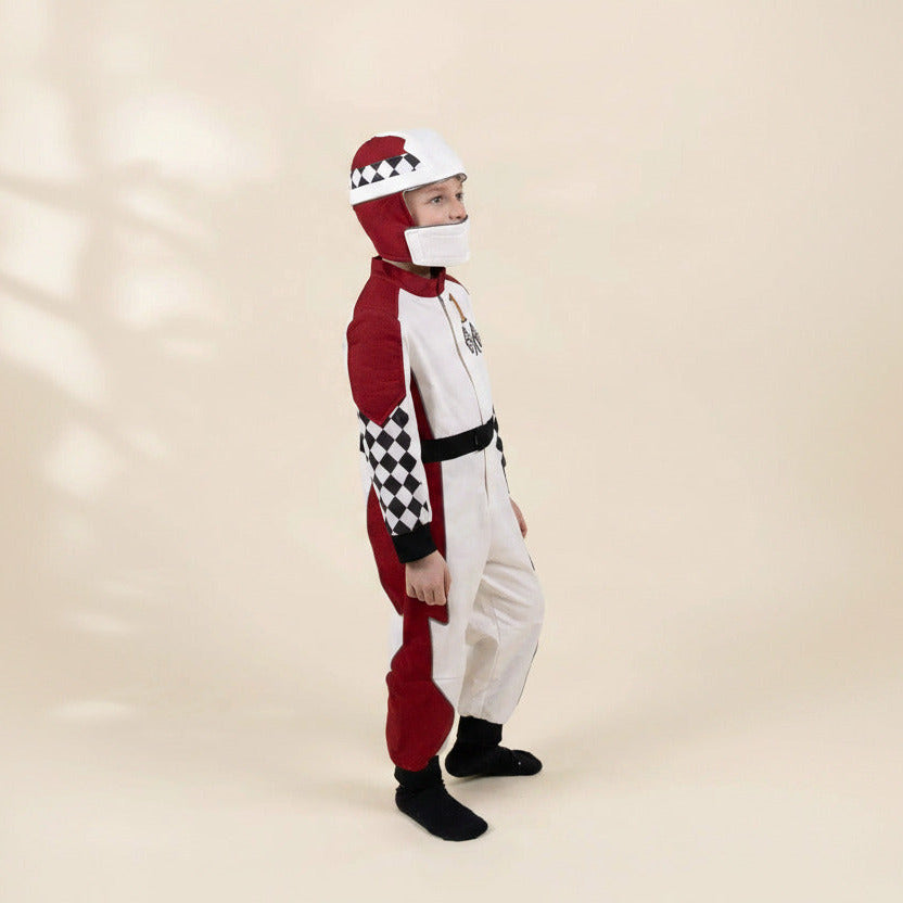 A child wearing a red and white racing-style costume jumpsuit with black-and-white checkered sleeve and hat details, standing against a plain beige studio background.