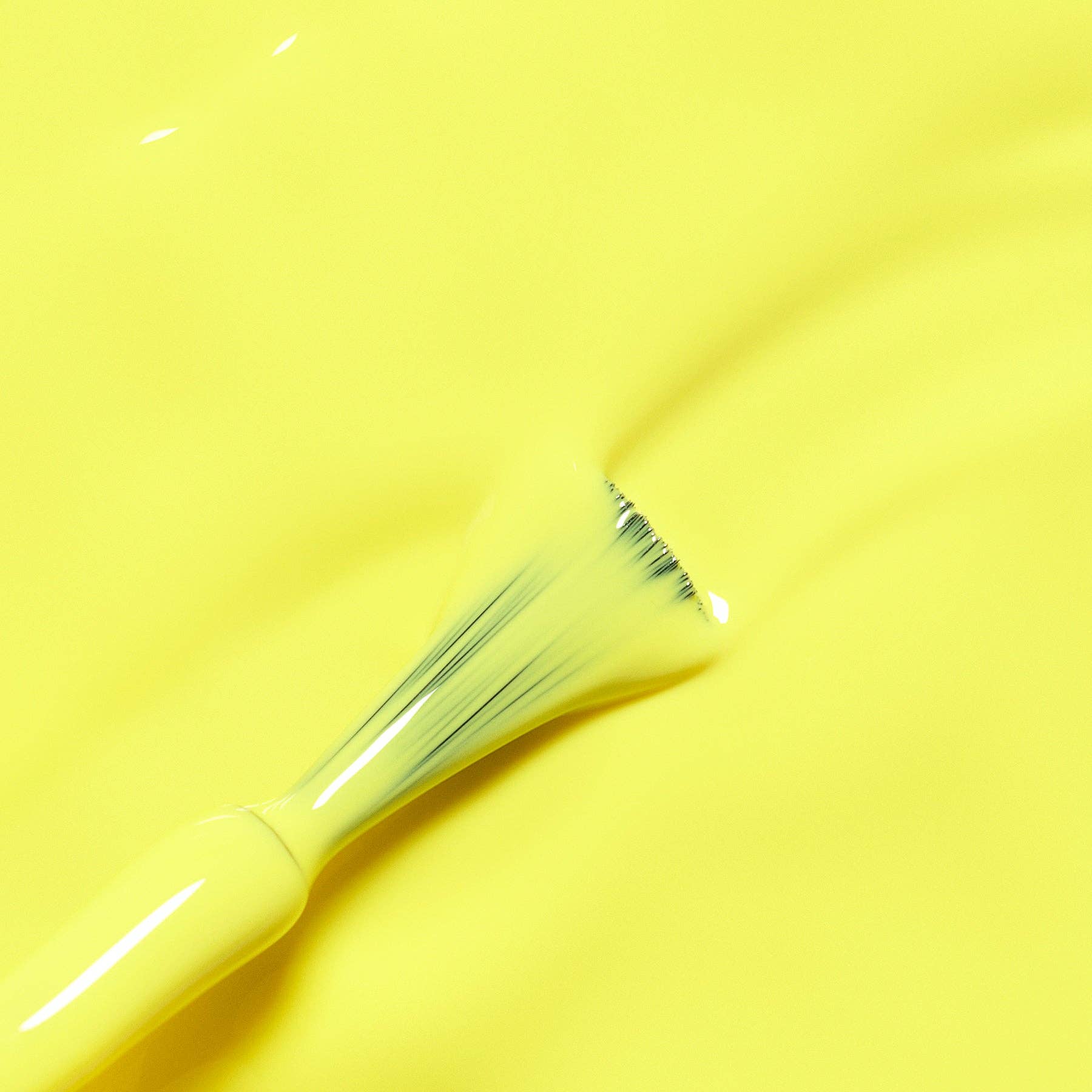 A close-up of a glossy bright yellow paint or cream texture with a small angled brush applying or blending the surface.