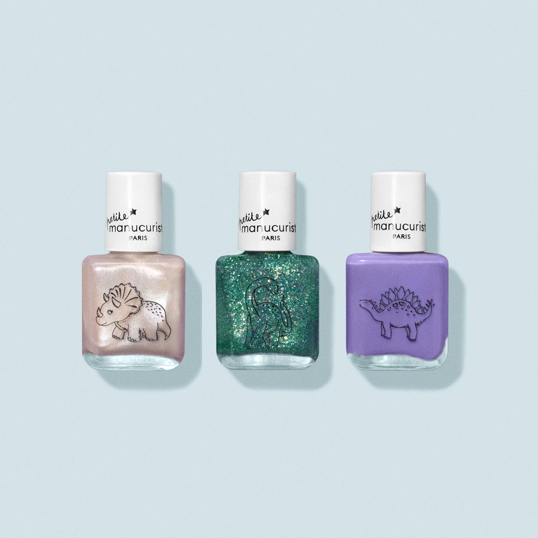 Three nail polish bottles with dinosaur designs on a light blue background
