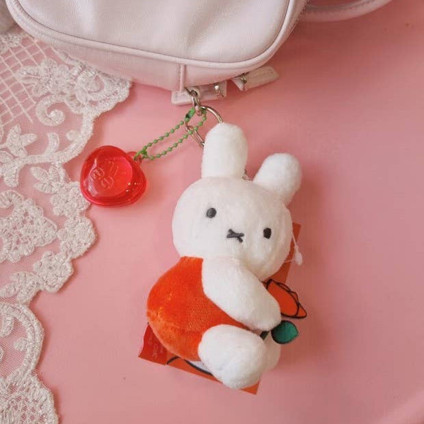 White plush keychain with a red bag on a pink surface with lace