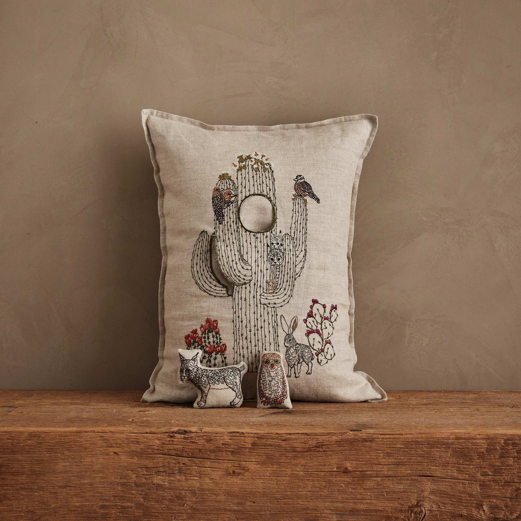 Decorative pillow with cactus and animal designs on a wooden surface against a brown background