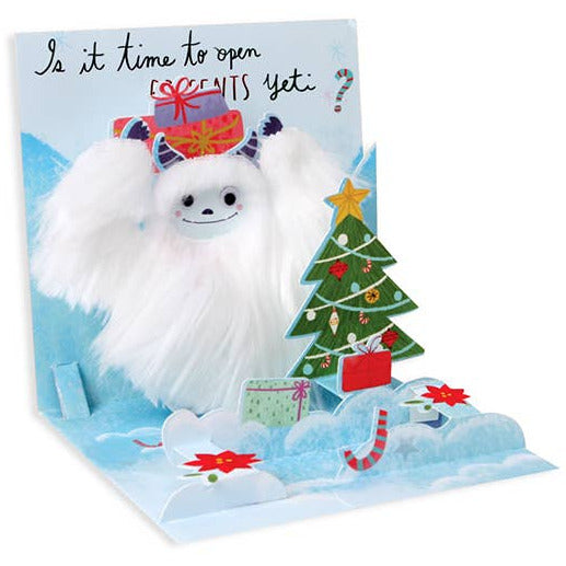 Christmas card with a fluffy white creature, Christmas tree, and presents on a blue background.