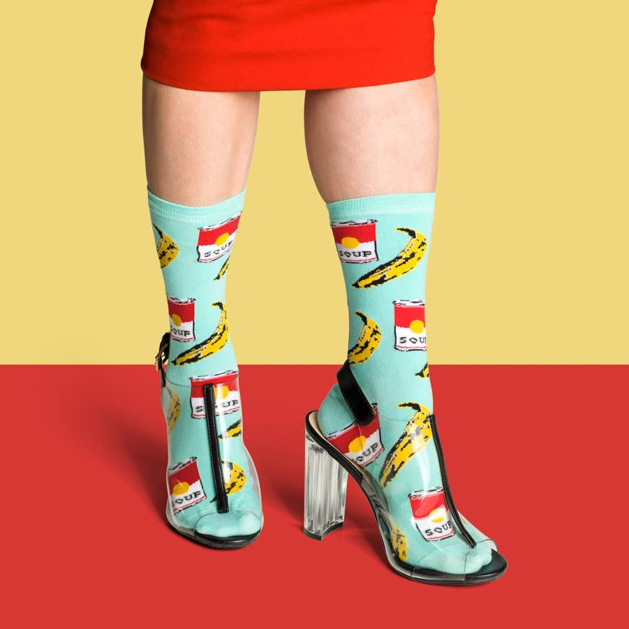 Person wearing light blue socks with banana and can design on a red and yellow background