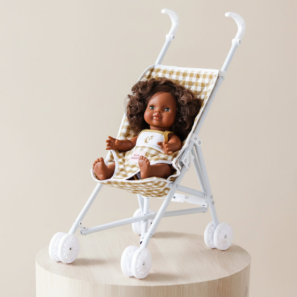 Doll sitting in a small white stroller with a checkered seat on a light gray background