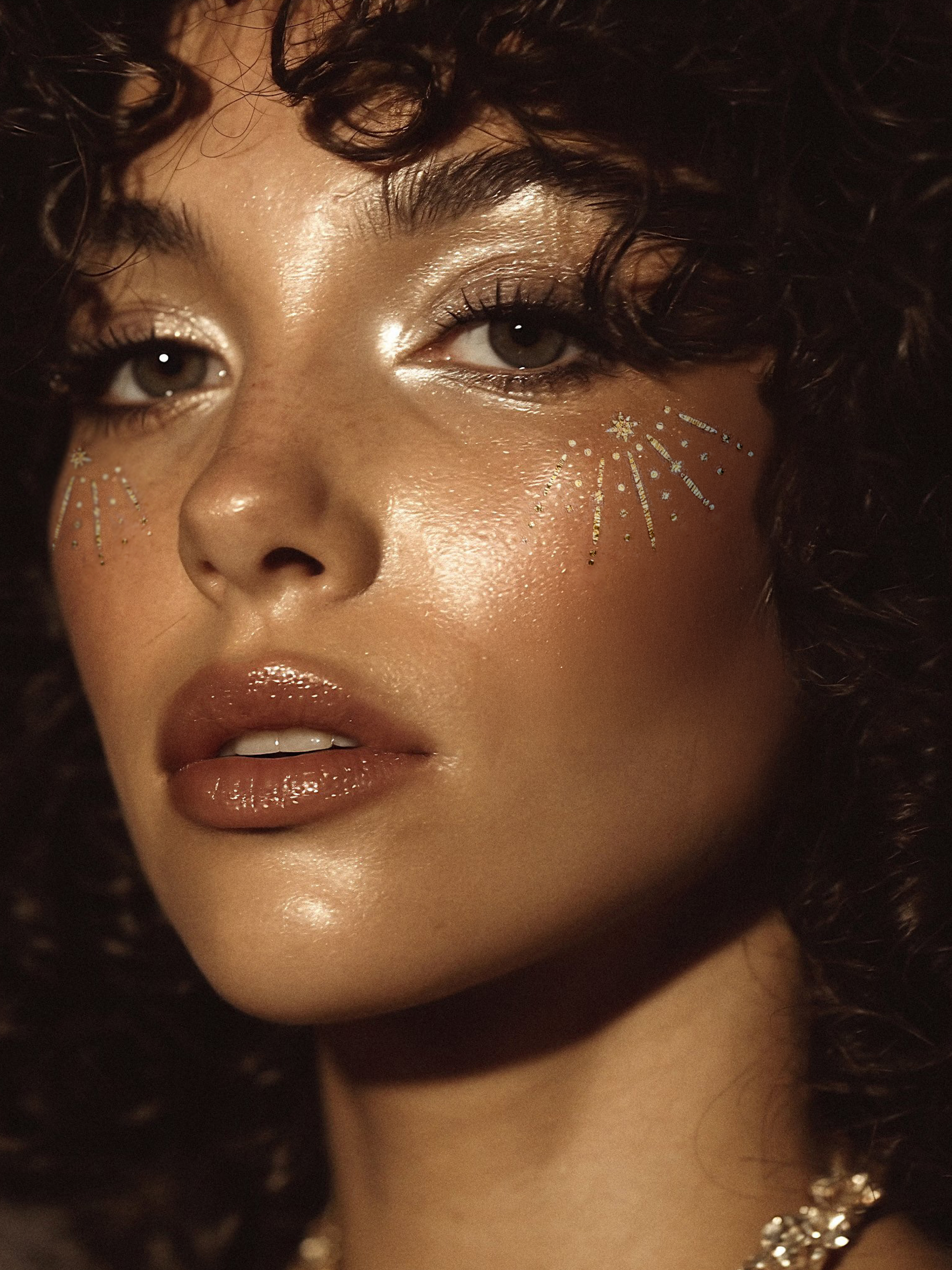 Close-up of a person with glittery makeup and curly hair.