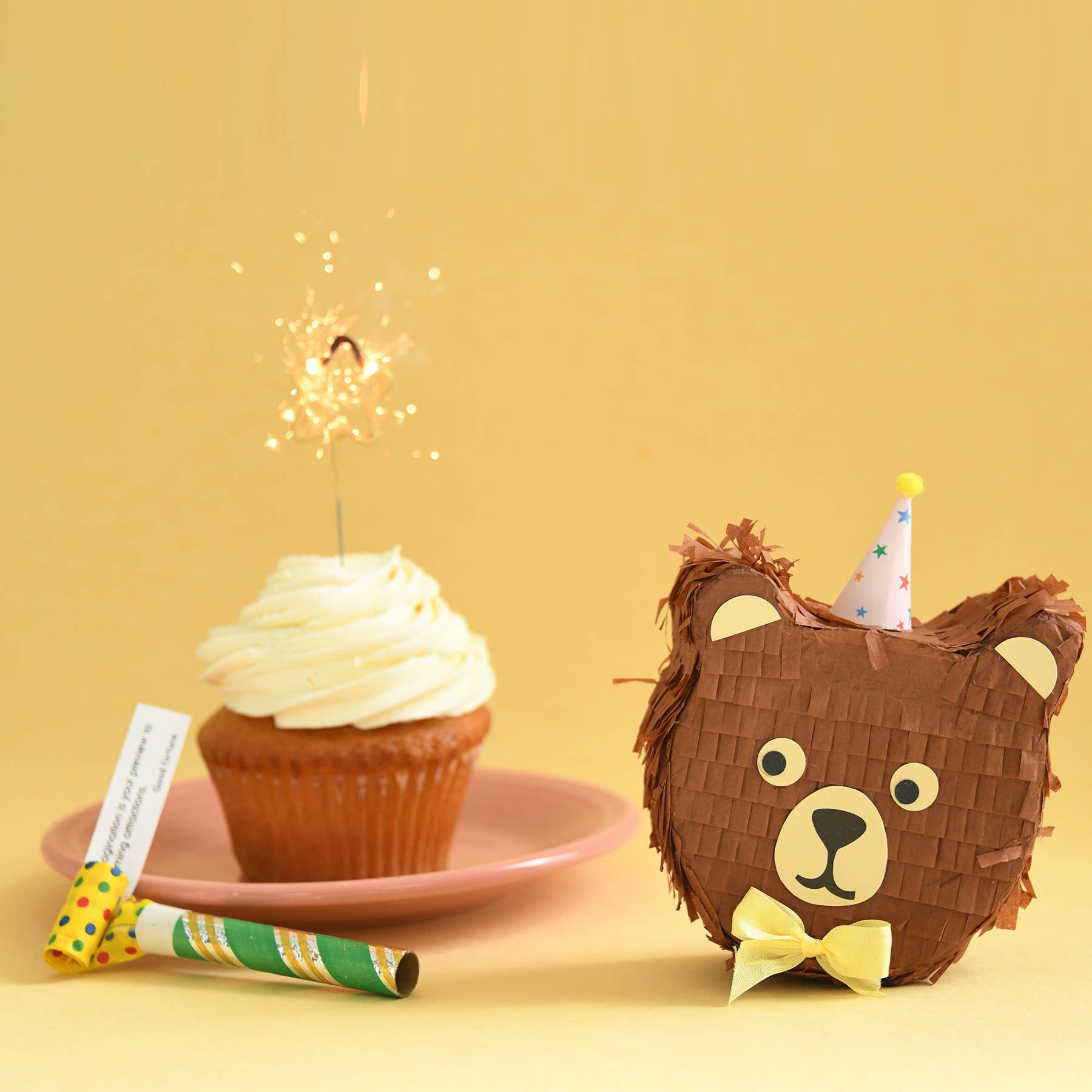 Bear-shaped piñata with cupcake and sparkler on yellow background