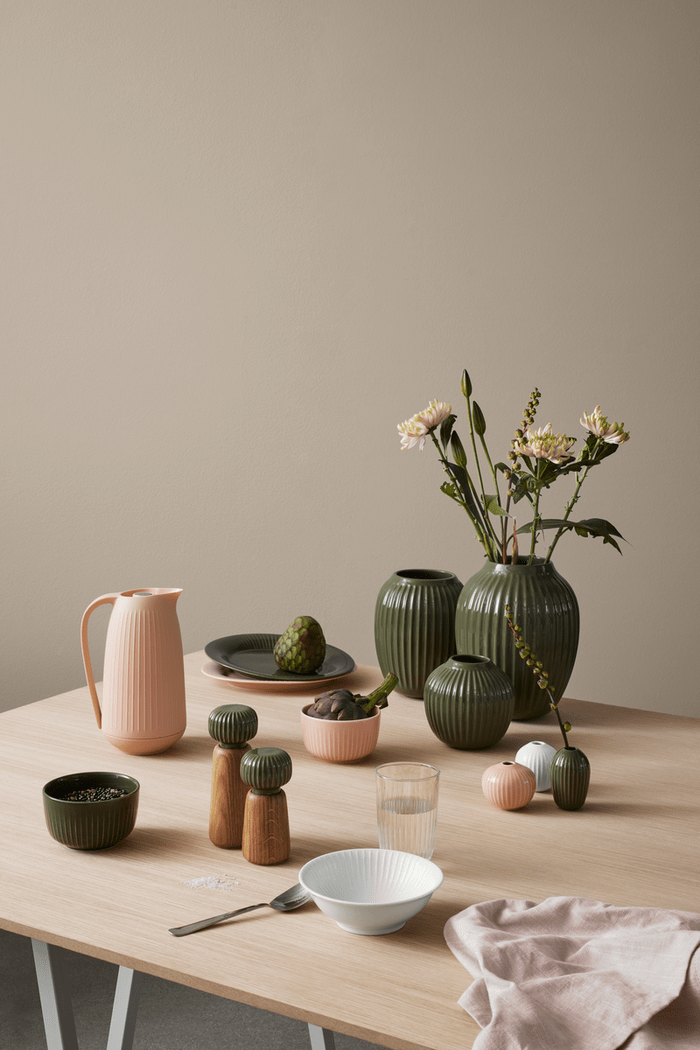 Table with ceramic and glassware including vases, bowls, and a pitcher against a beige wall.