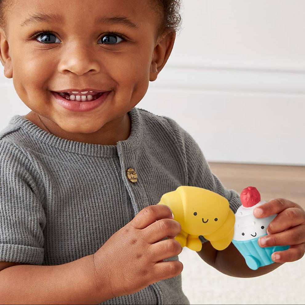 Child holding two colorful bath toys, one yellow and one blue, against a neutral background.