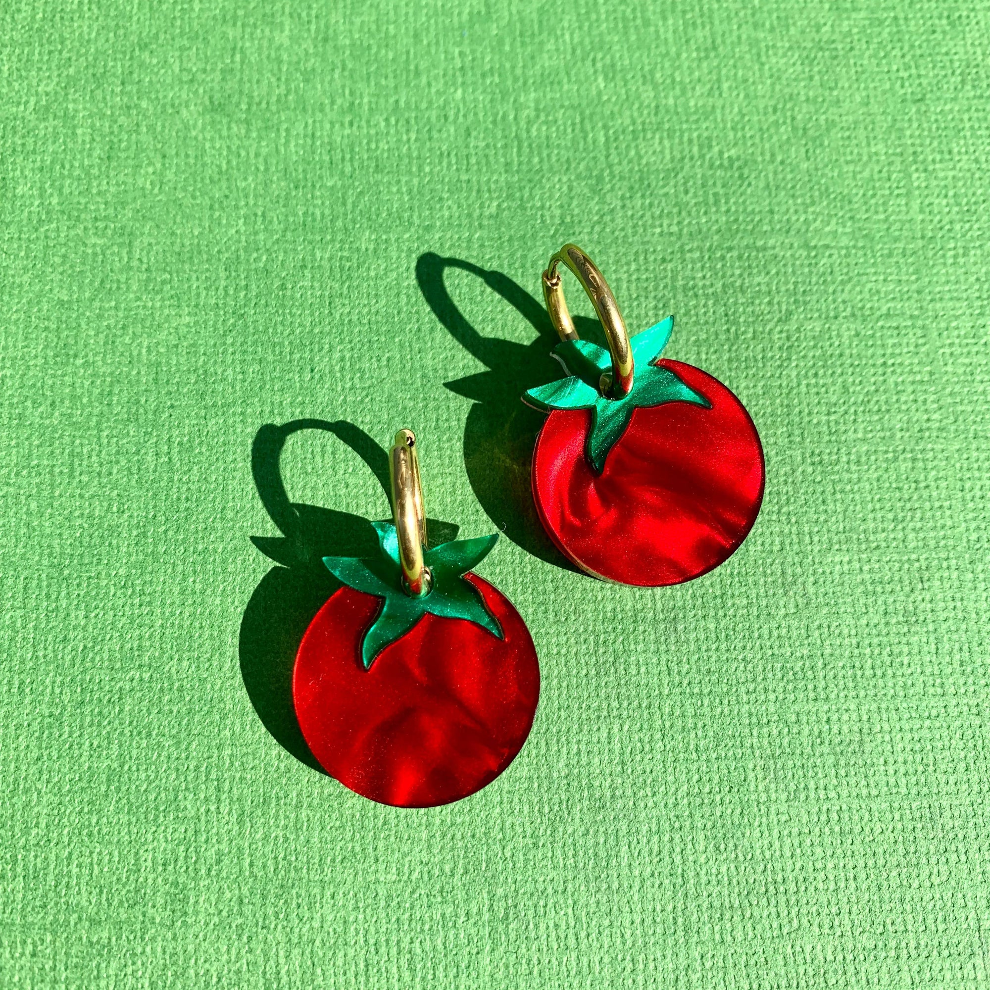 Red tomato-shaped earrings with green leaves on a green background