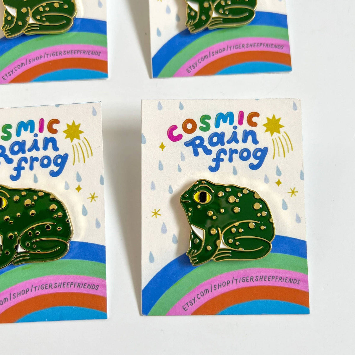 Green frog pin with 'Cosmic Rain Frog' packaging on a white background