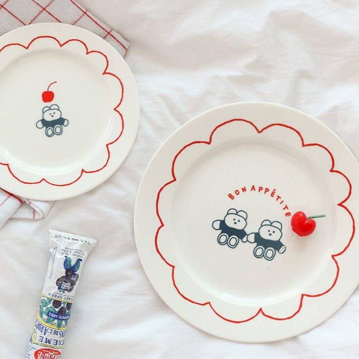 Two decorative plates with cartoon designs on a white surface with a red and white checkered cloth.