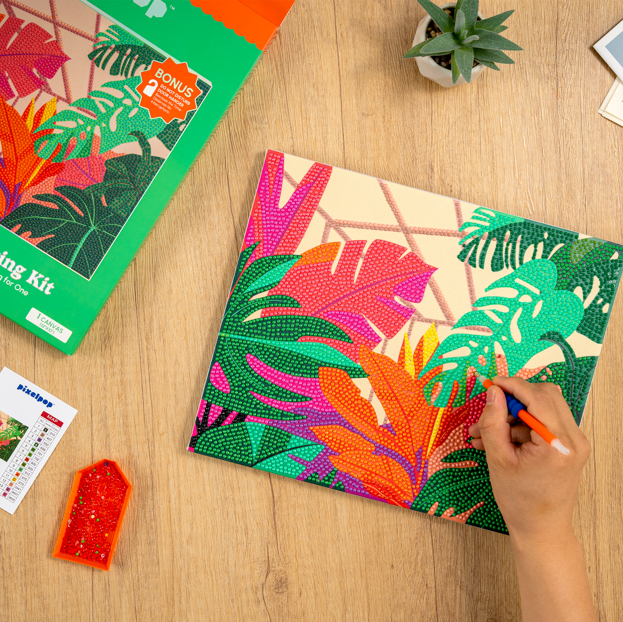 Colorful mosaic art project on a wooden table with a hand using a tool.