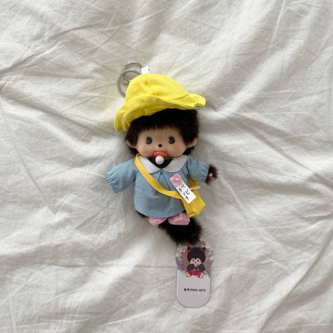 Small plush toy with a yellow hat and blue outfit on a white fabric background