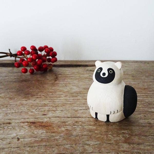 Small white and black animal figurine on a wooden surface with red berries in the background