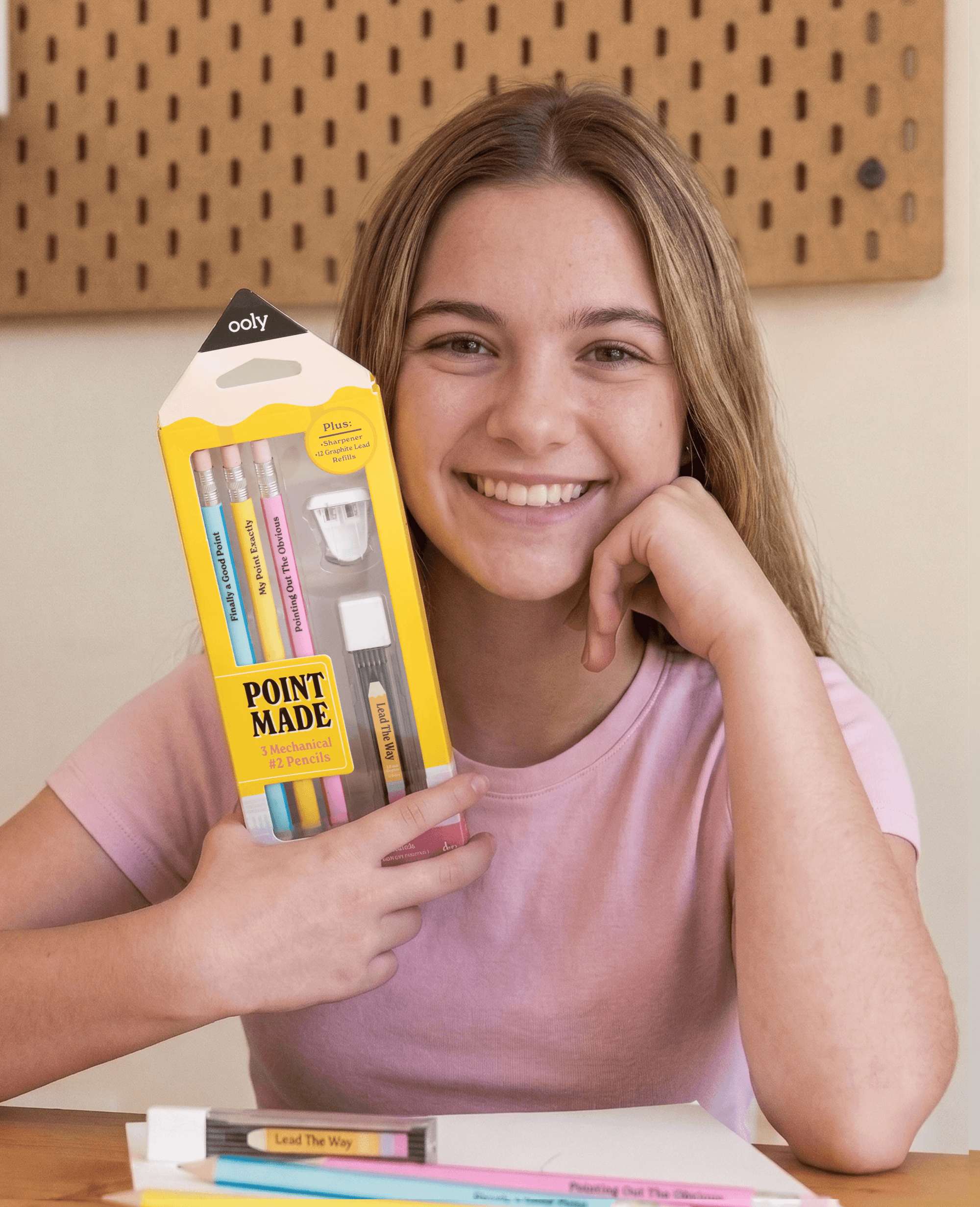 Young girl holding a package of markers with a smile, sitting at a table.