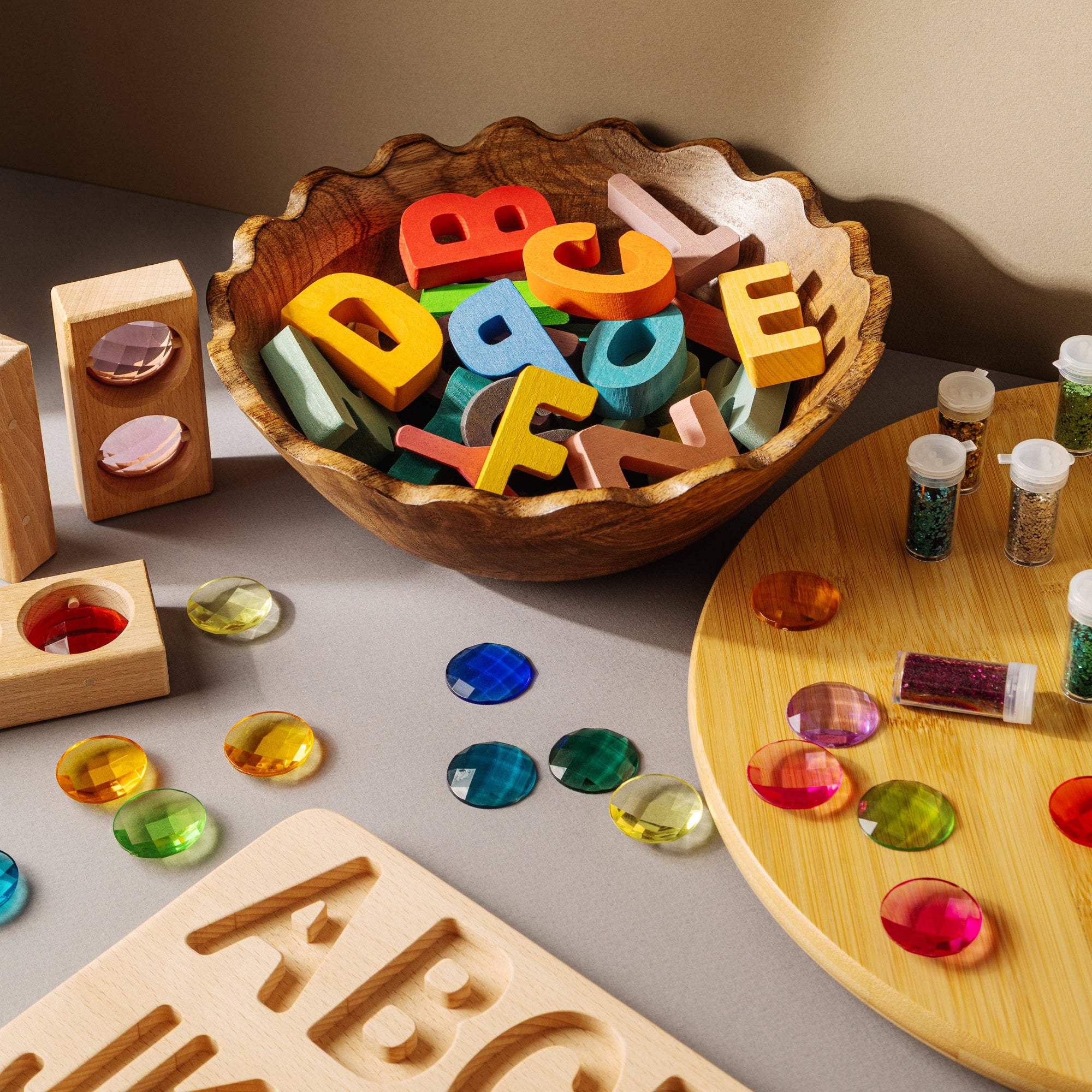 Colorful wooden letters in a bowl with educational toys on a table