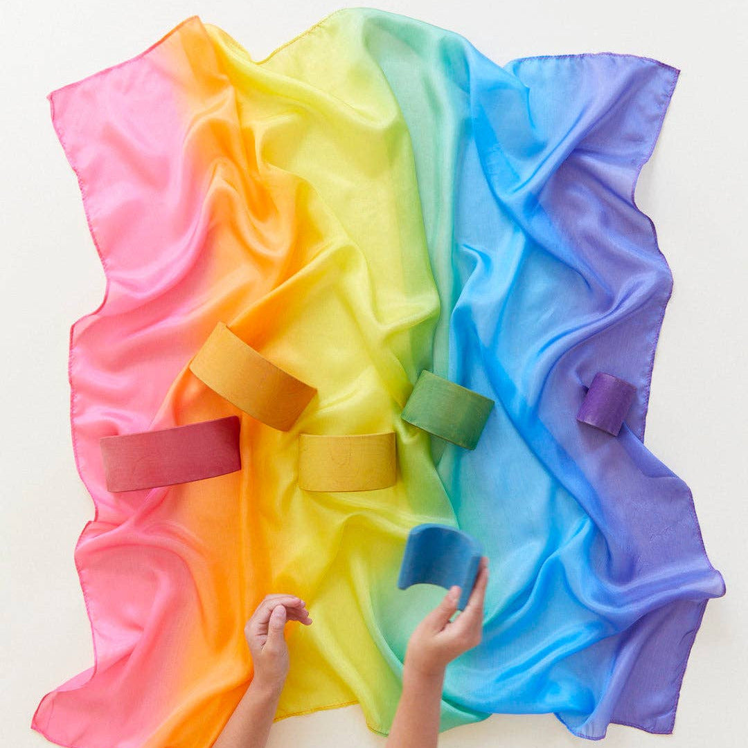 Colorful rainbow cape with children's hands holding it on a white background