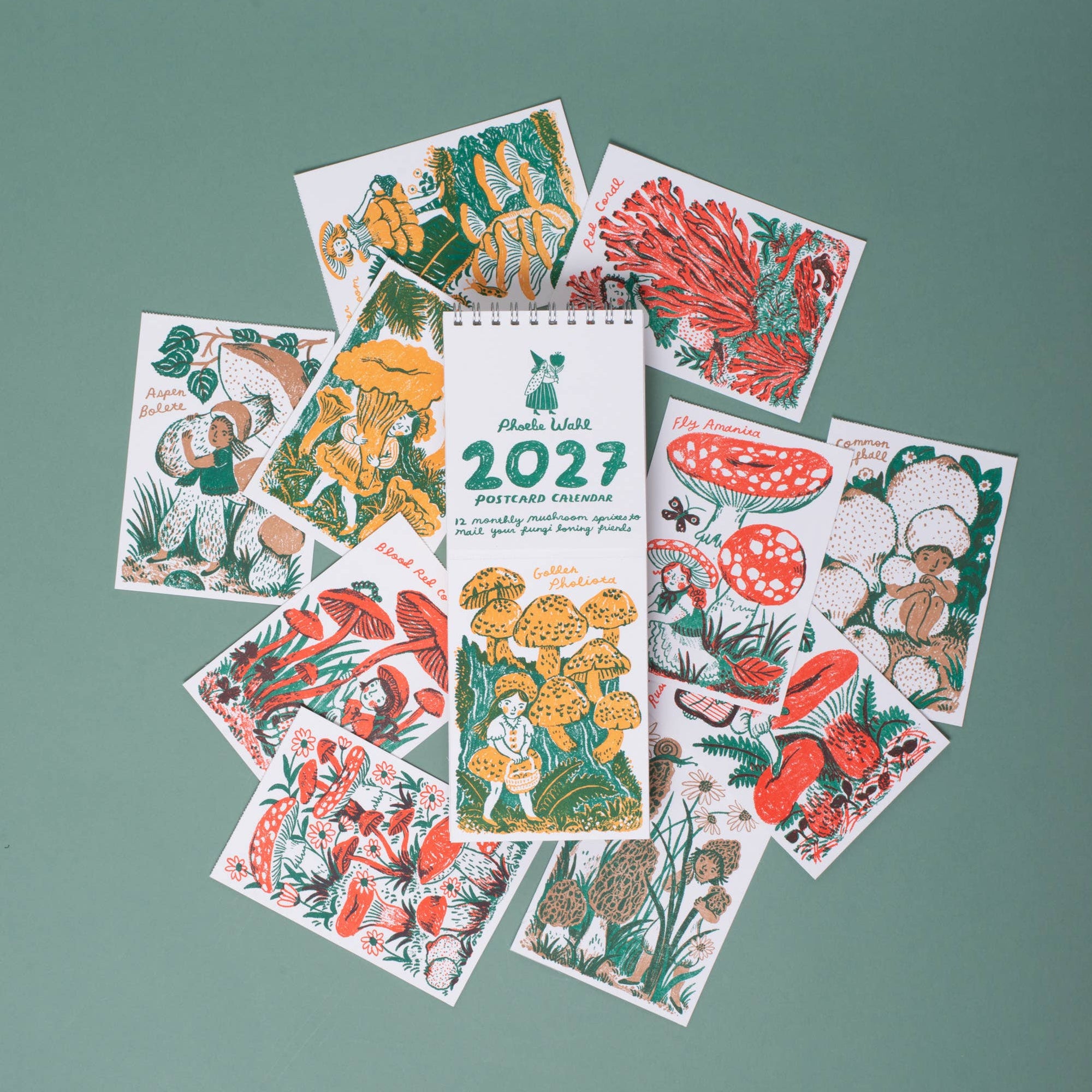 A spiral-bound 2027 mushroom-themed calendar or booklet lies centered on a muted green background, surrounded by several illustrated sample pages showing red, yellow, green, and brown botanical and mushroom drawings.