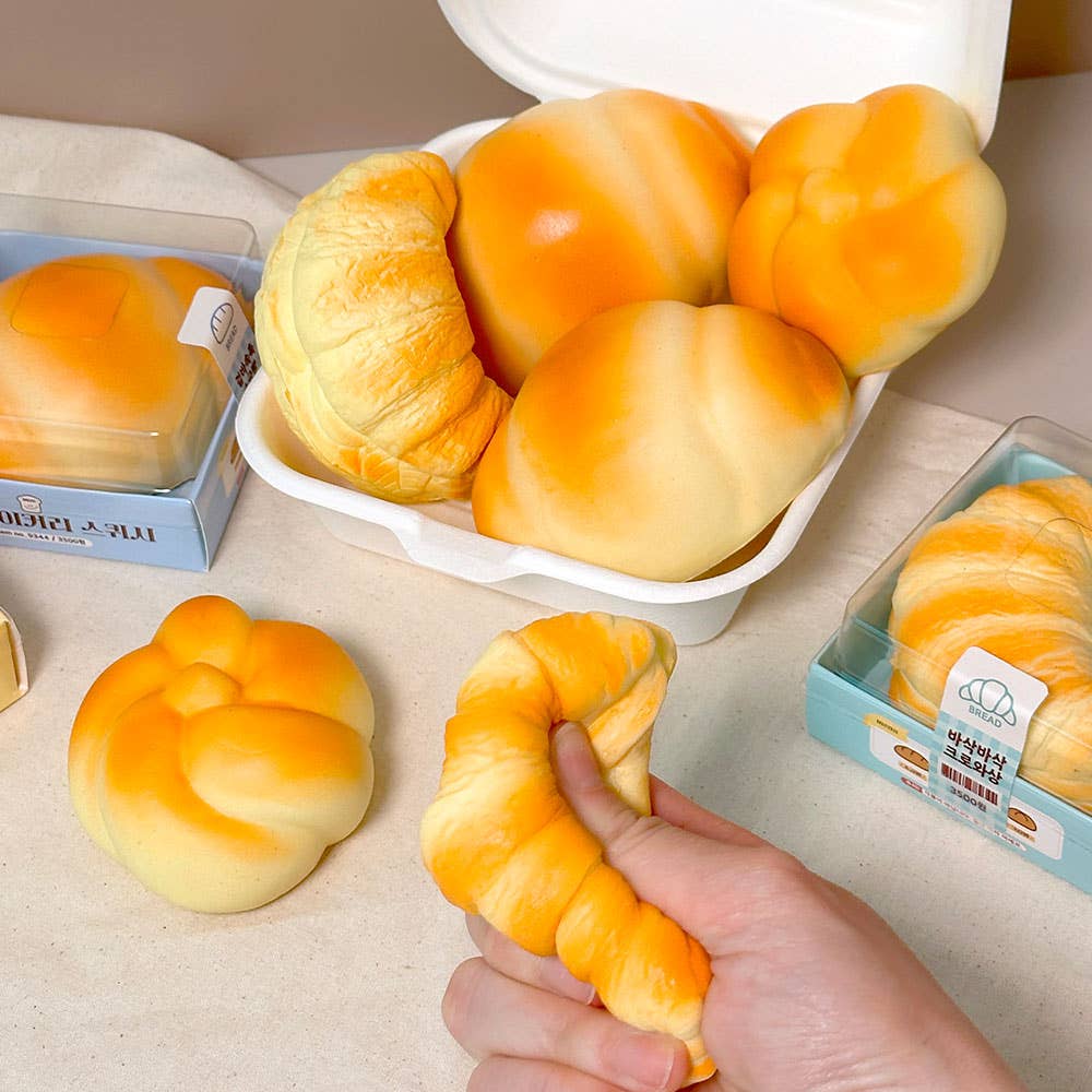 Baked goods in a white container with a hand holding a bread roll on a light surface.