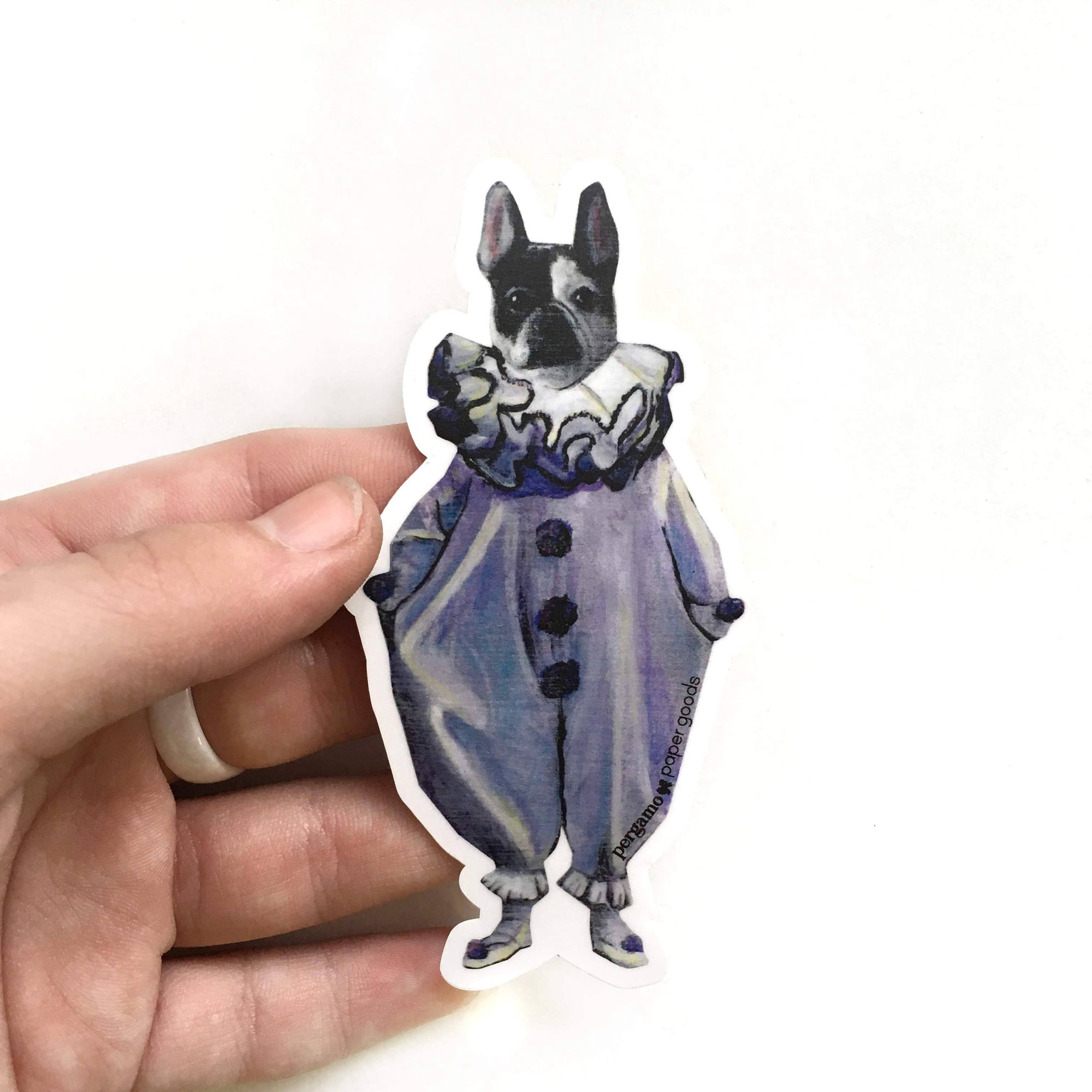 Hand holding a sticker of a dog in a purple outfit on a white background