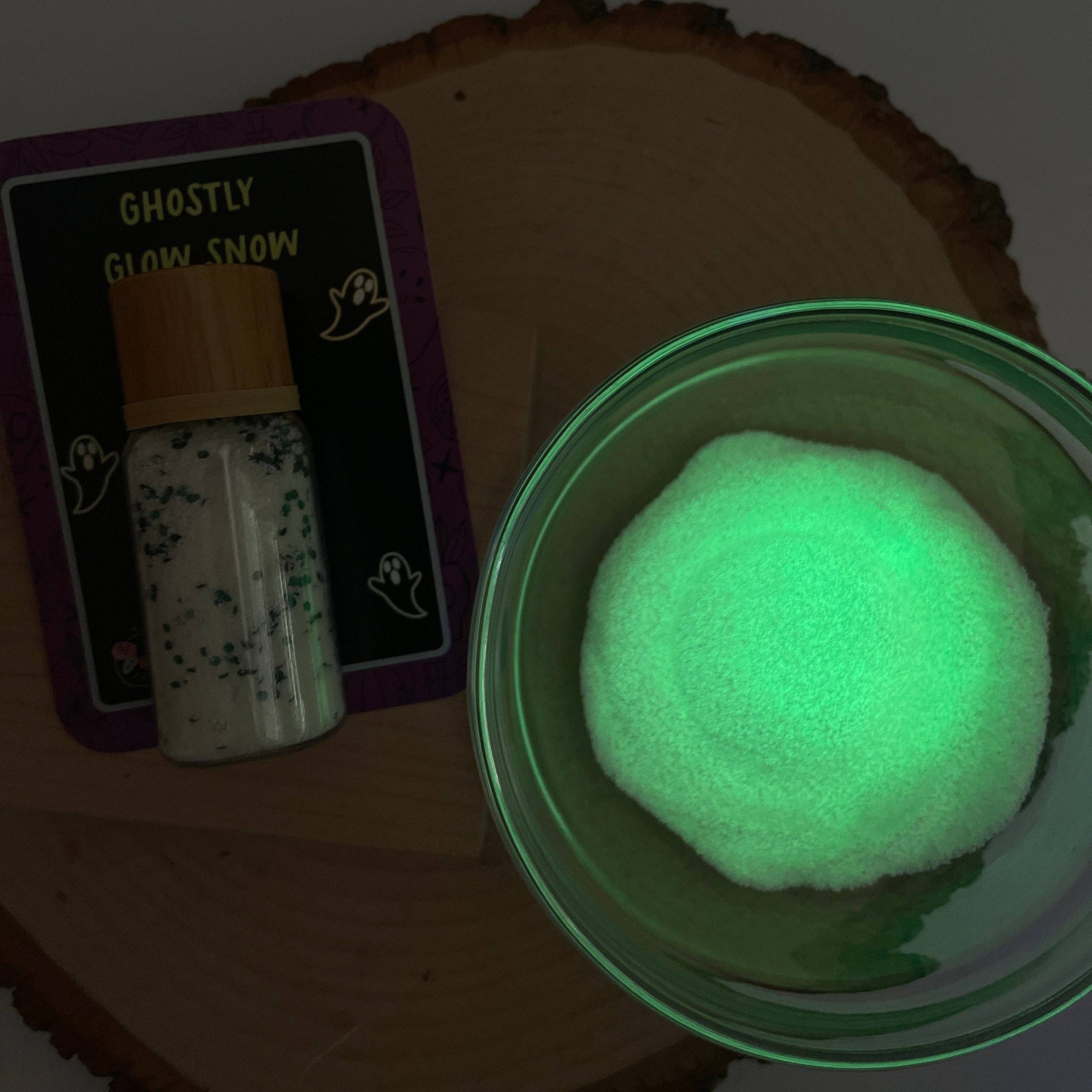 Glow-in-the-dark powder in a green container with packaging labeled 'Ghostly Glow Snow' on a wooden surface.