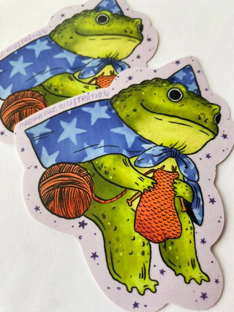 Two green frogs with yarn and a blue scarf on a white background