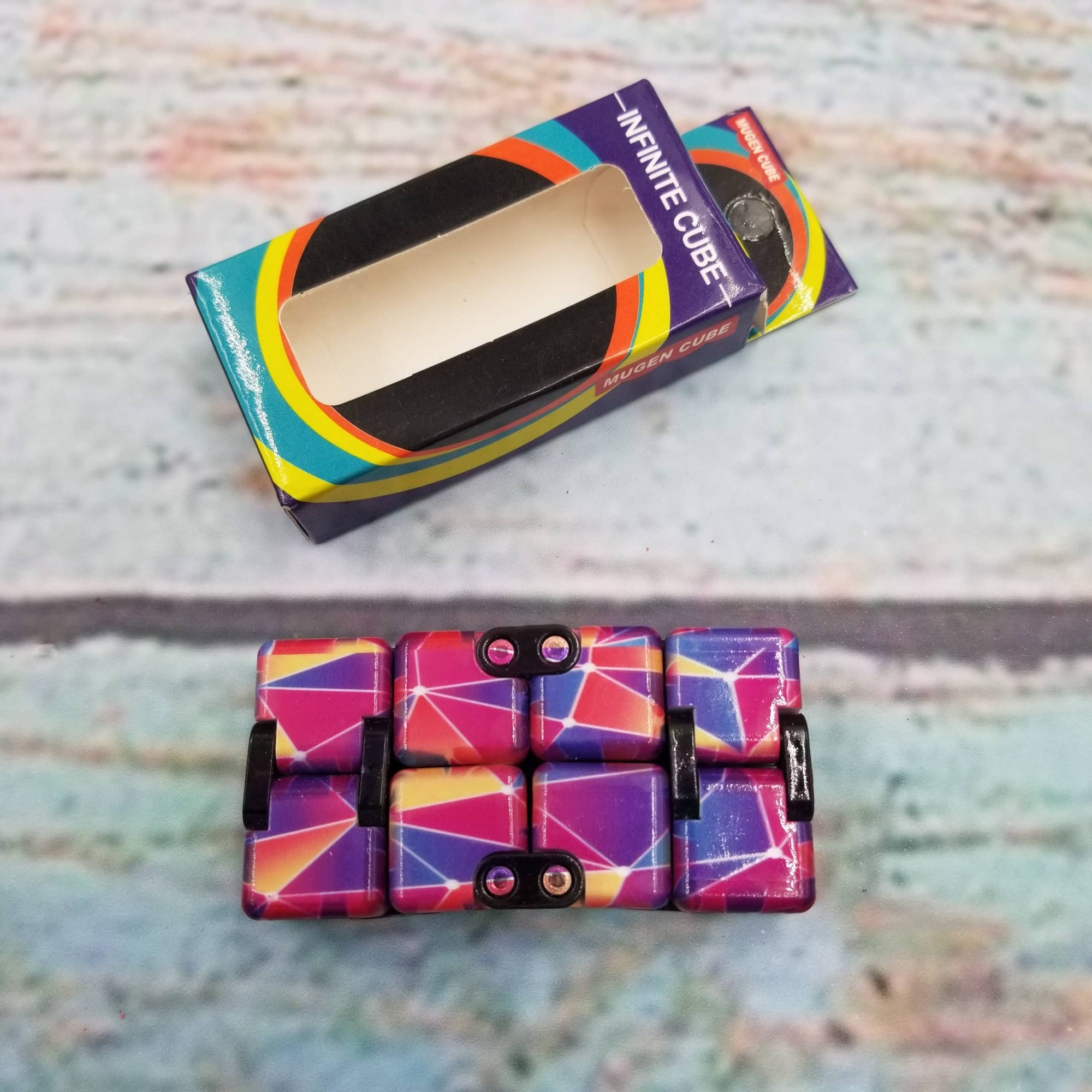 Colorful geometric-patterned Infinite Cube toy with packaging on a textured surface