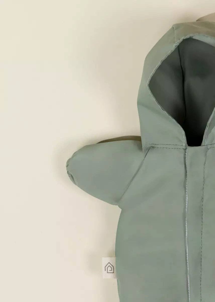 A close-up of a sage green hooded jacket or soft accessory with a gray inner lining, shown against a plain off-white background.