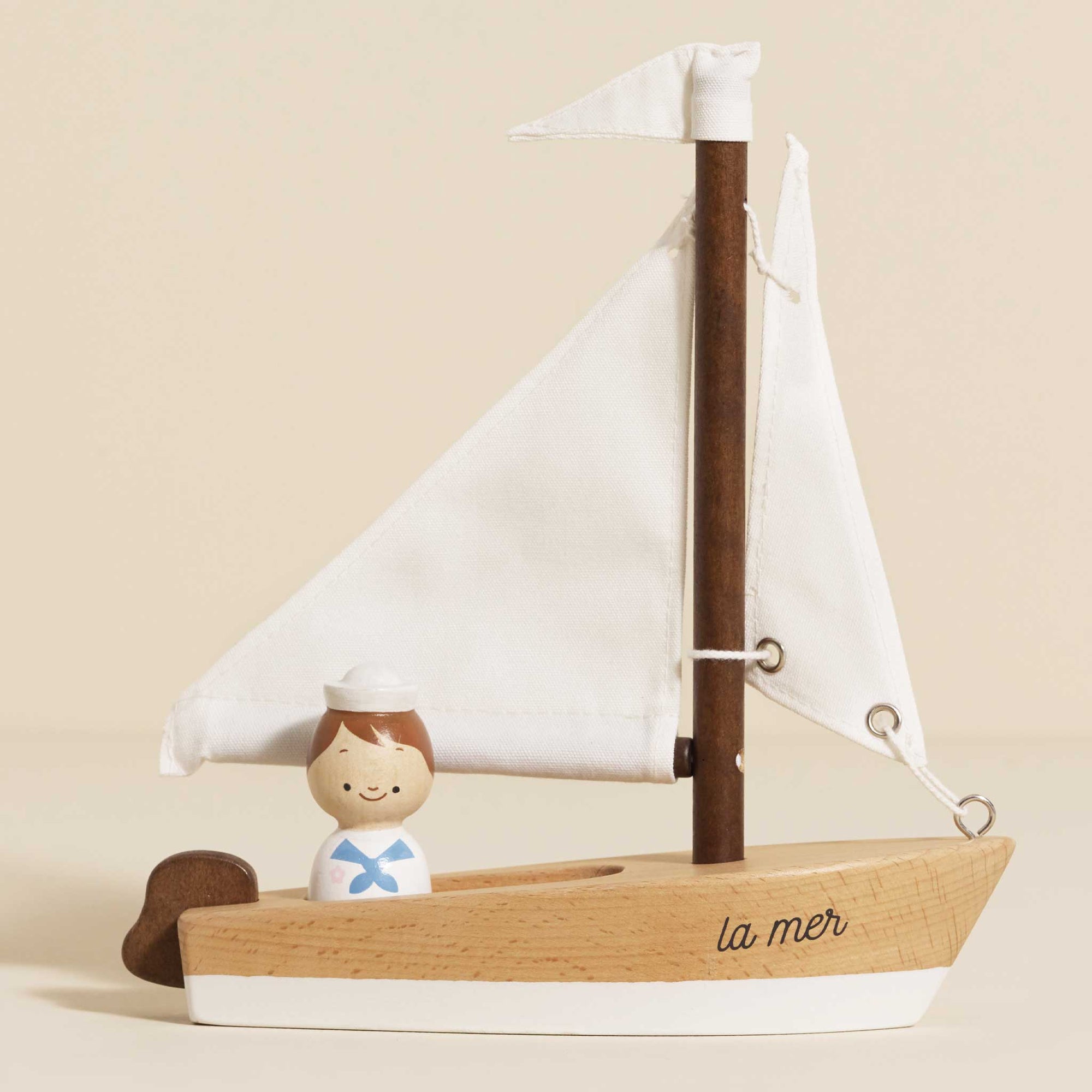 Wooden sailboat model with a small figure of a sailor on a beige background