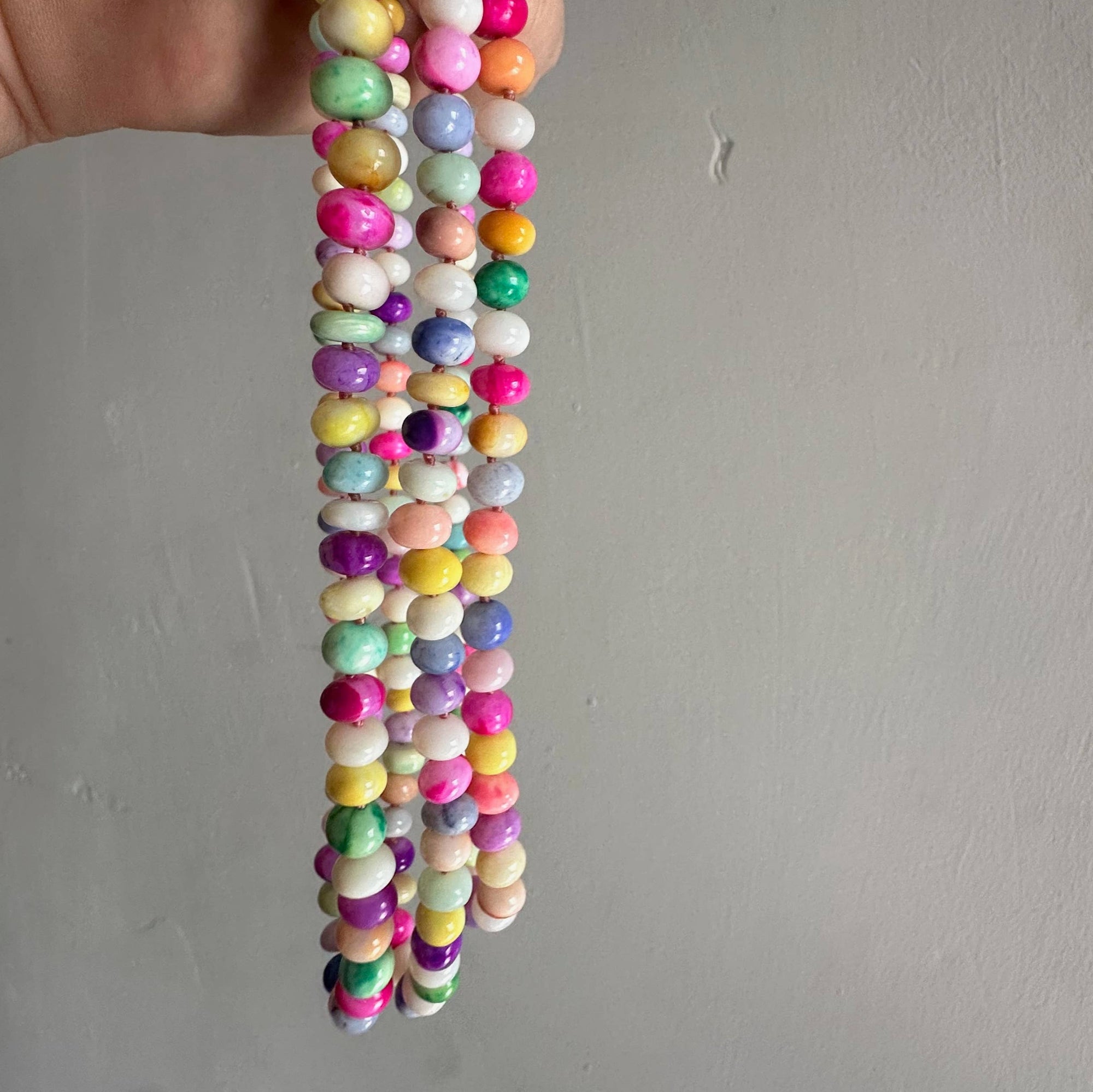 Colorful beaded necklace held by a hand against a plain background