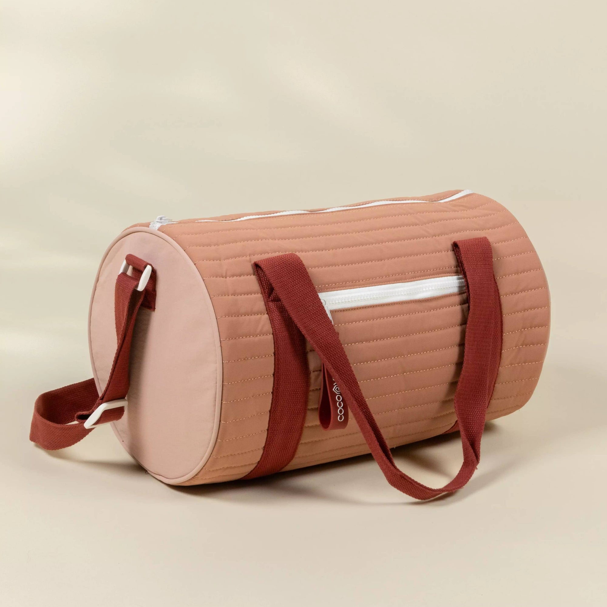 Pink duffel bag with red straps on a beige background