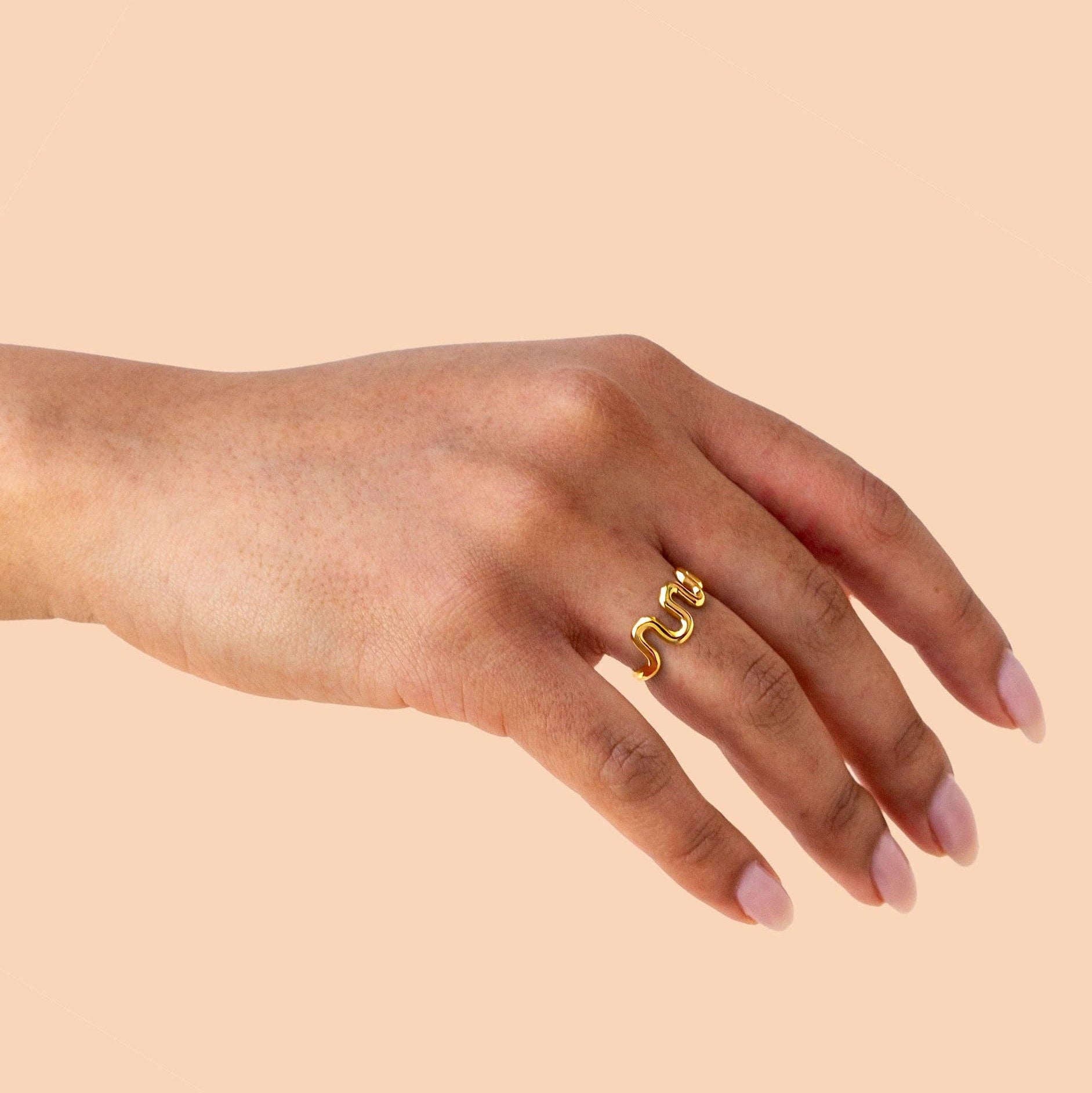 Hand wearing a gold ring on a beige background