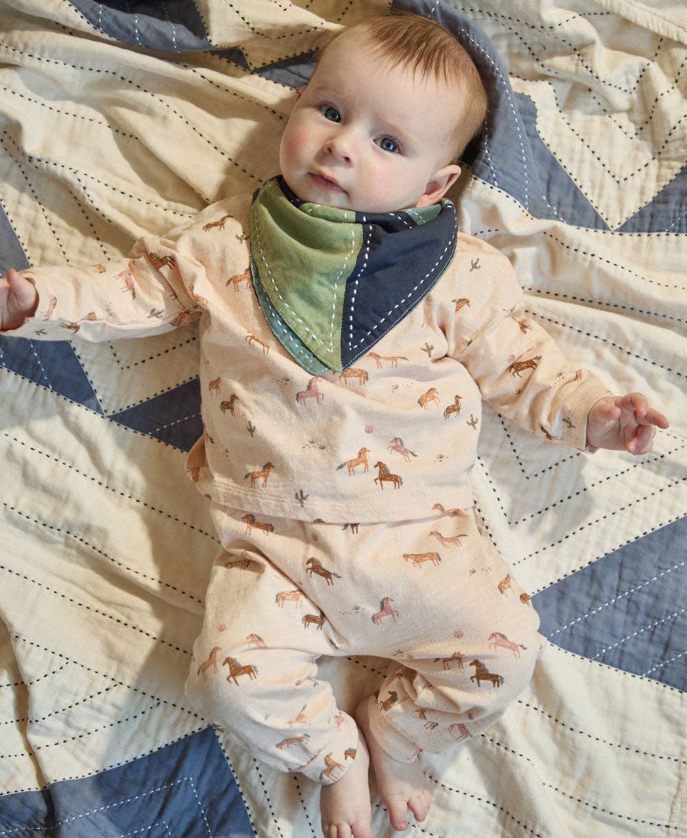 Baby wearing a patterned onesie and green bib on a quilted blanket