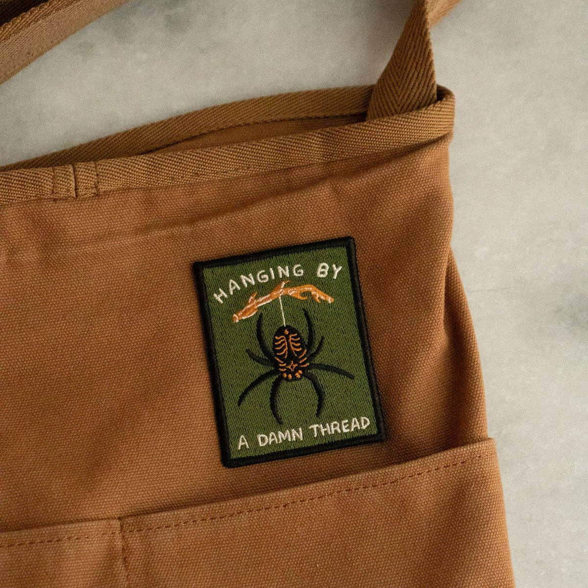 Brown bag with a patch featuring a spider design and text on a neutral background