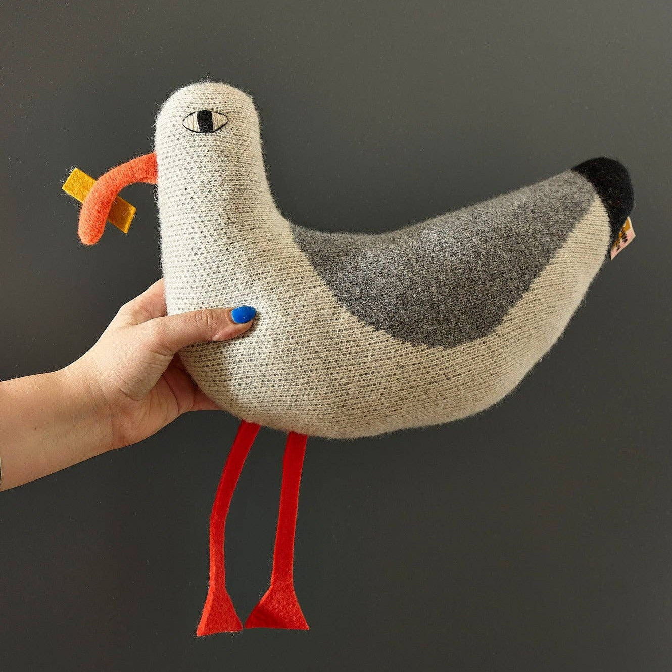 Hand holding a knitted seagull toy against a dark background