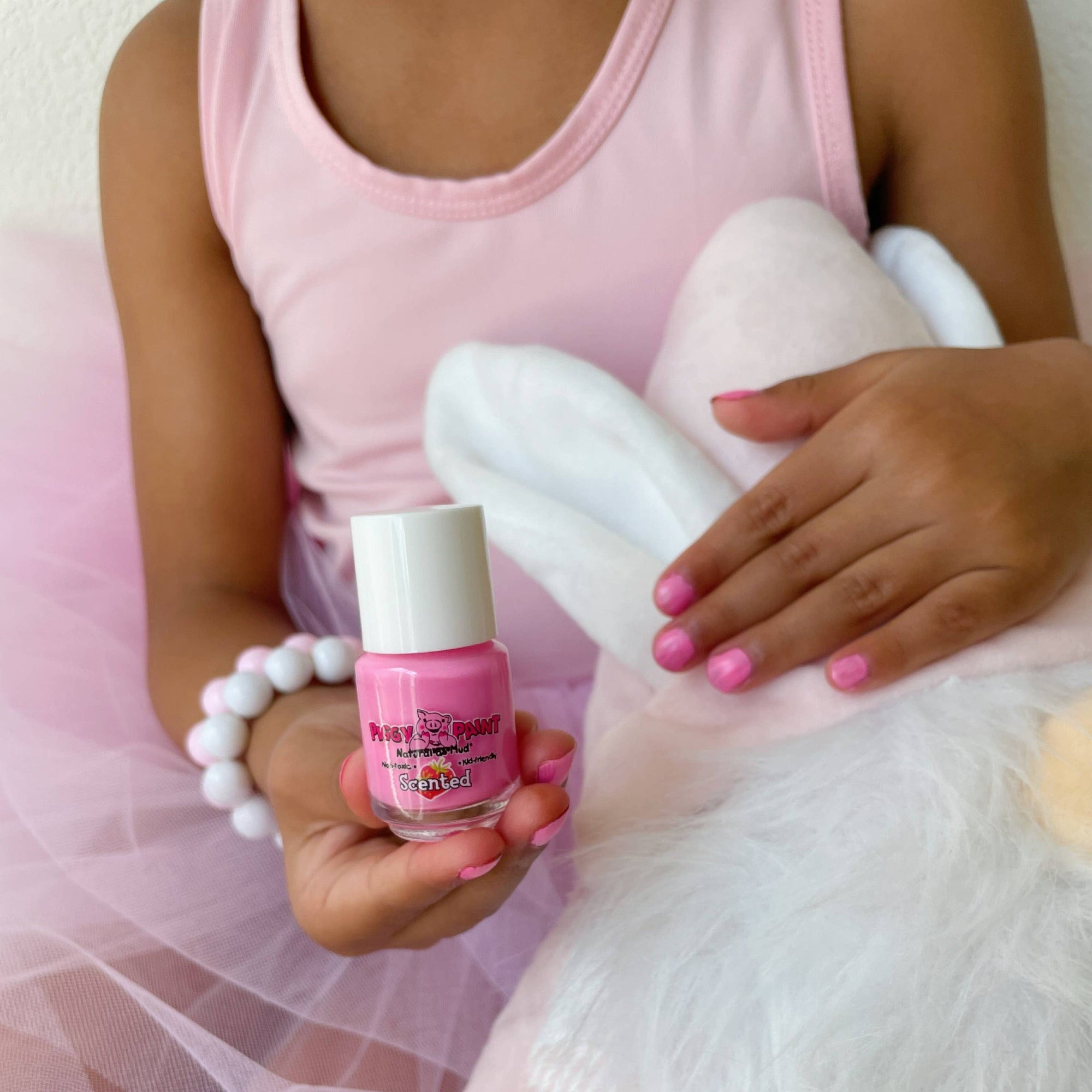 Child holding a bottle of pink nail polish and a white balloon with a pink heart.