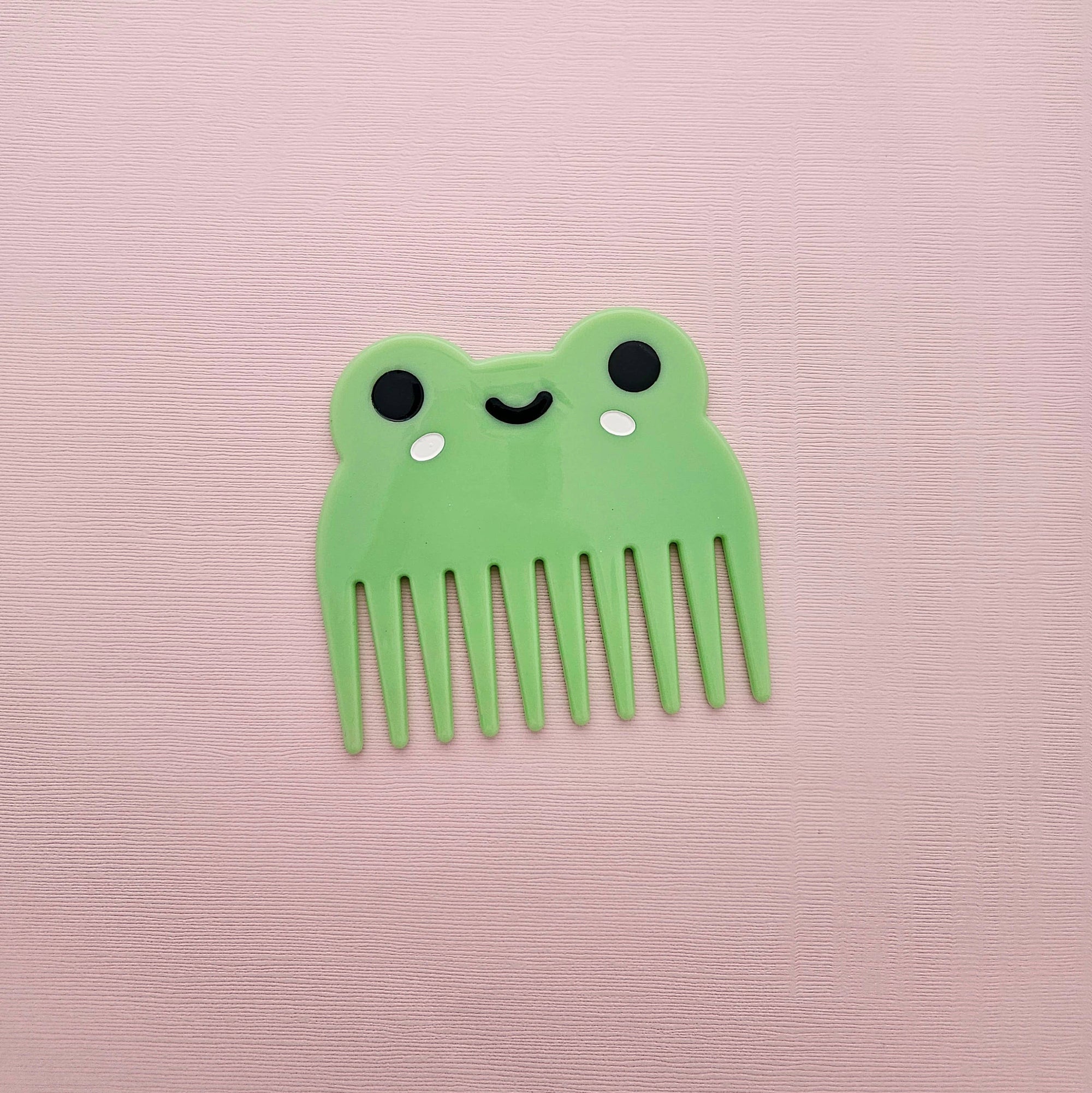 Green comb with a cute face design on a pink background