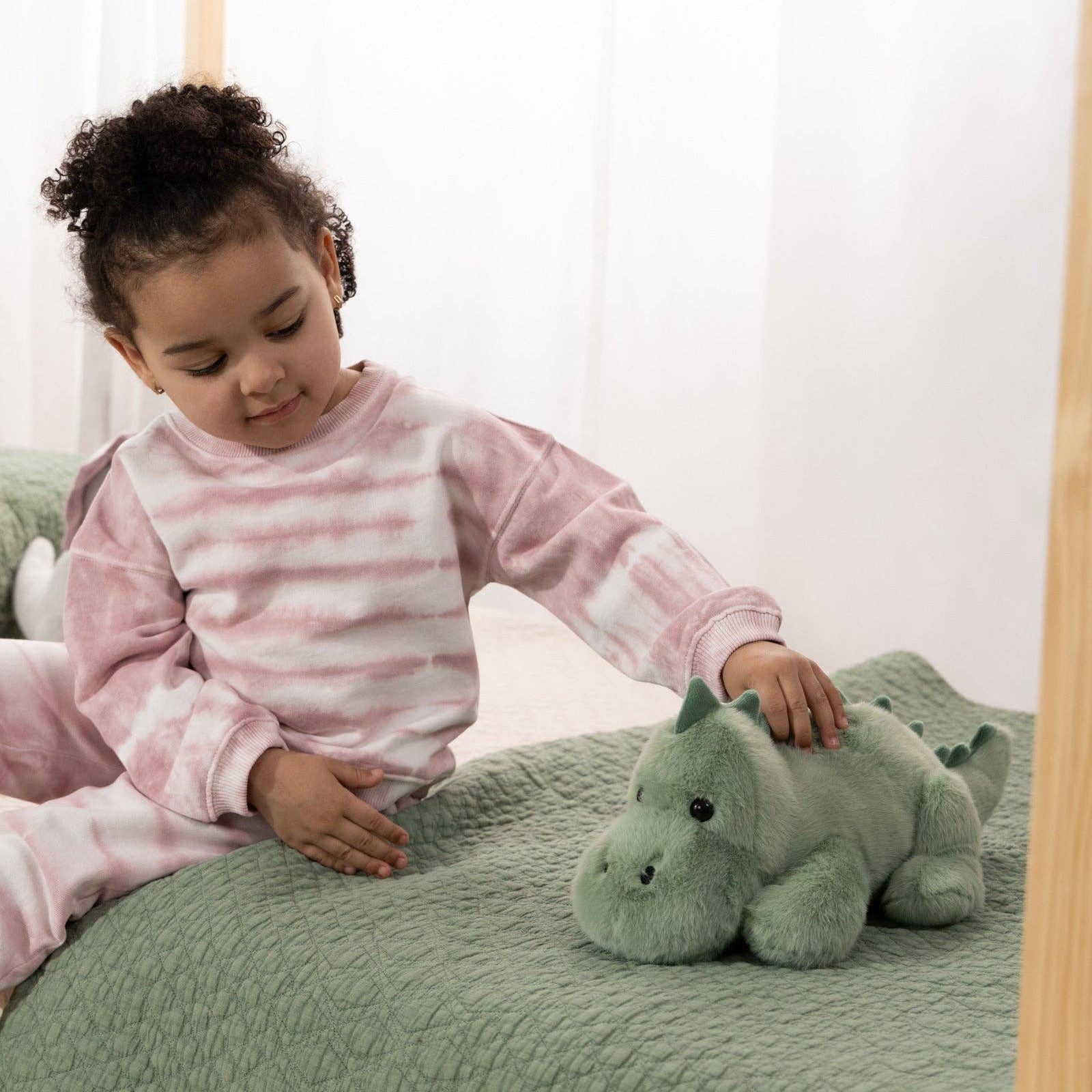 Child playing with a green plush toy on a bed