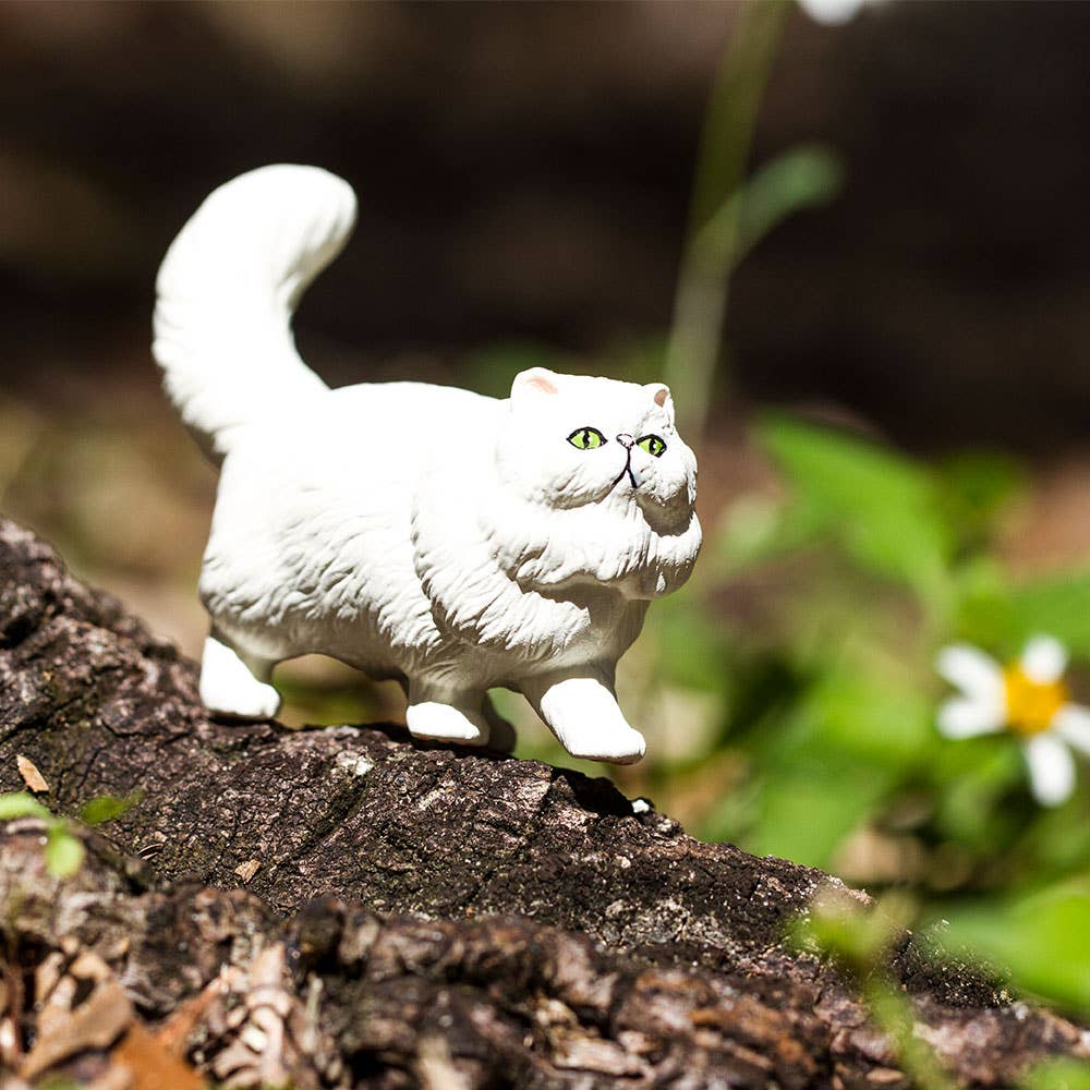 White cat figurine on a wooden log with blurred natural background