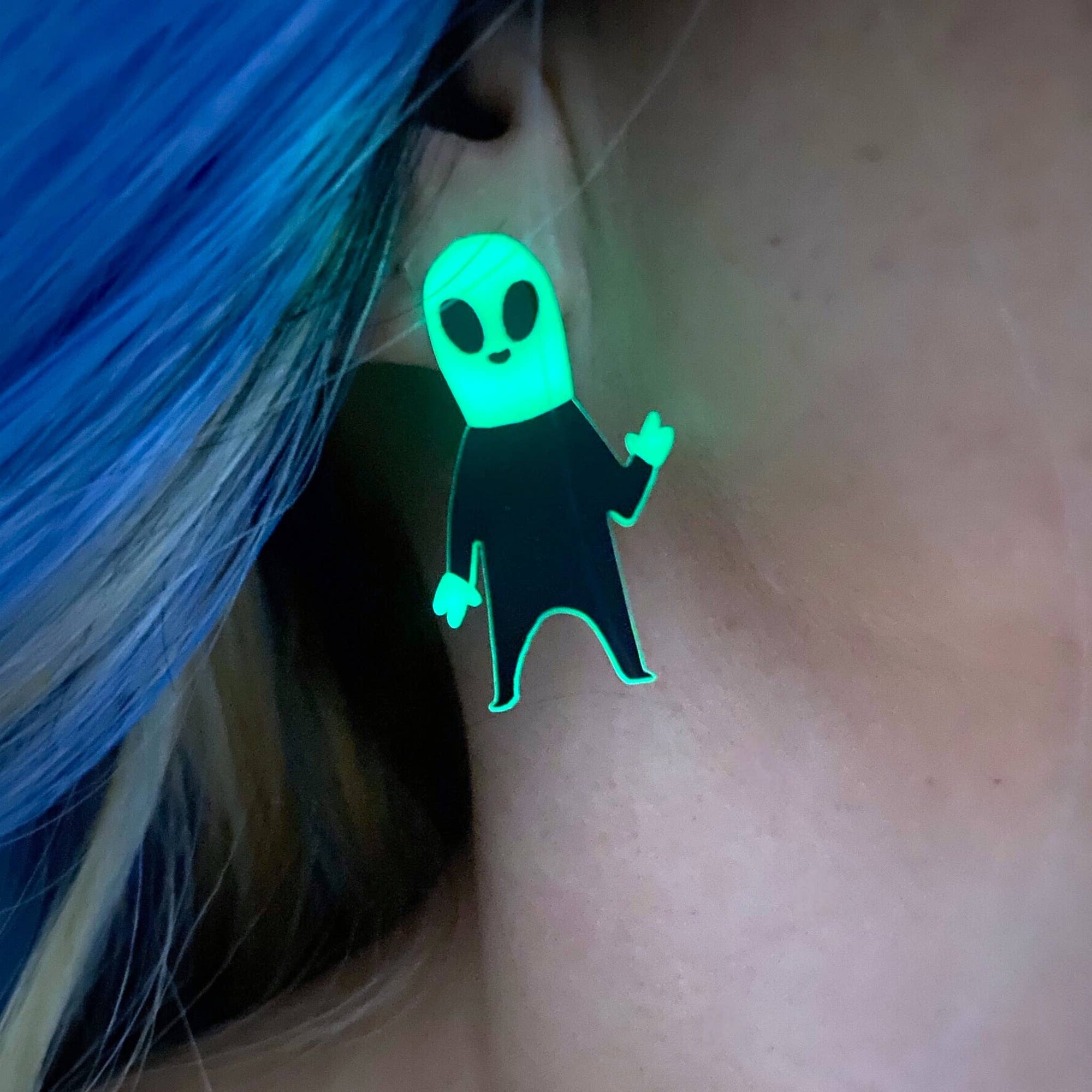 Glowing green alien-shaped earring worn on a person's ear.