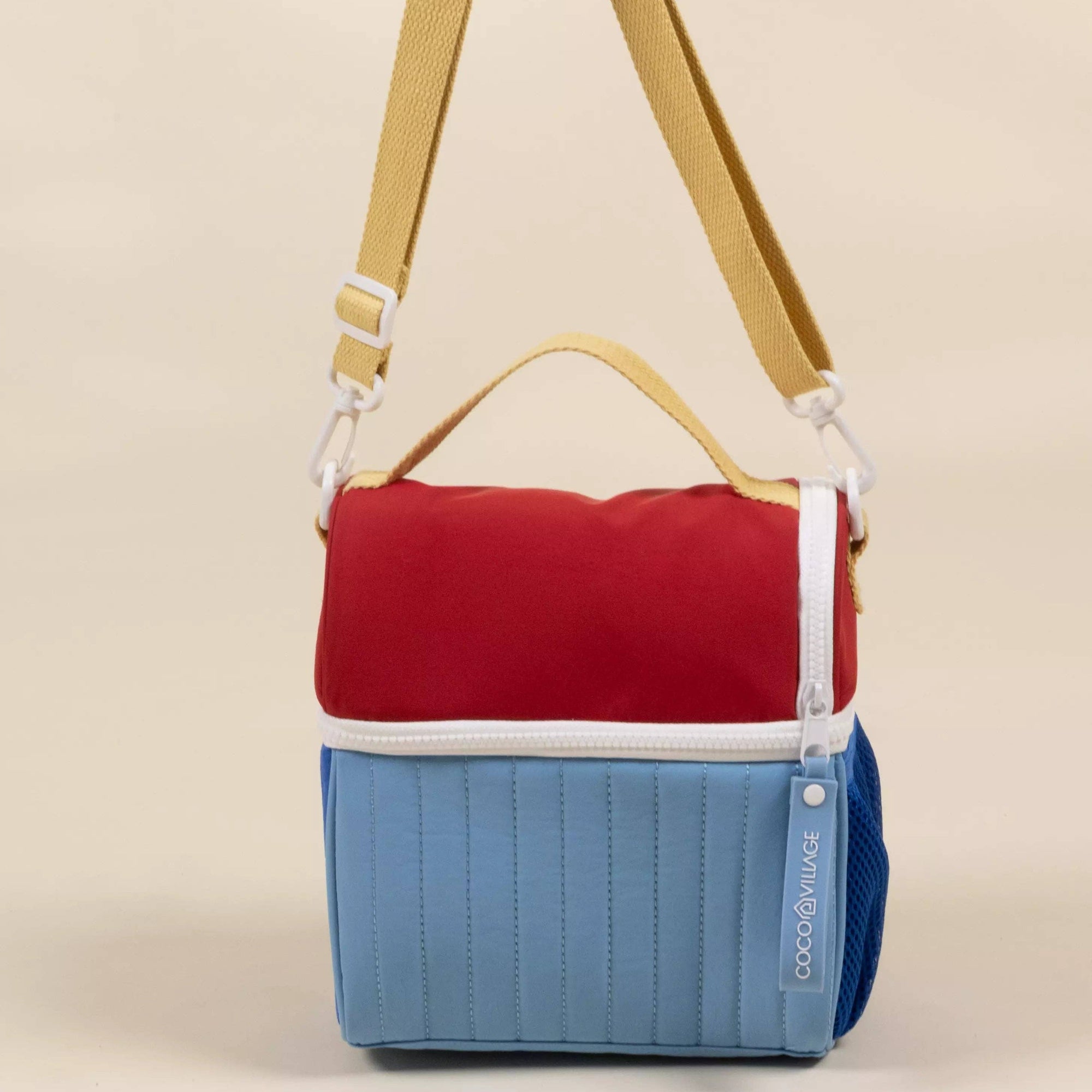 Multicolored bag with a red top section, blue bottom section, and yellow strap on a beige background
