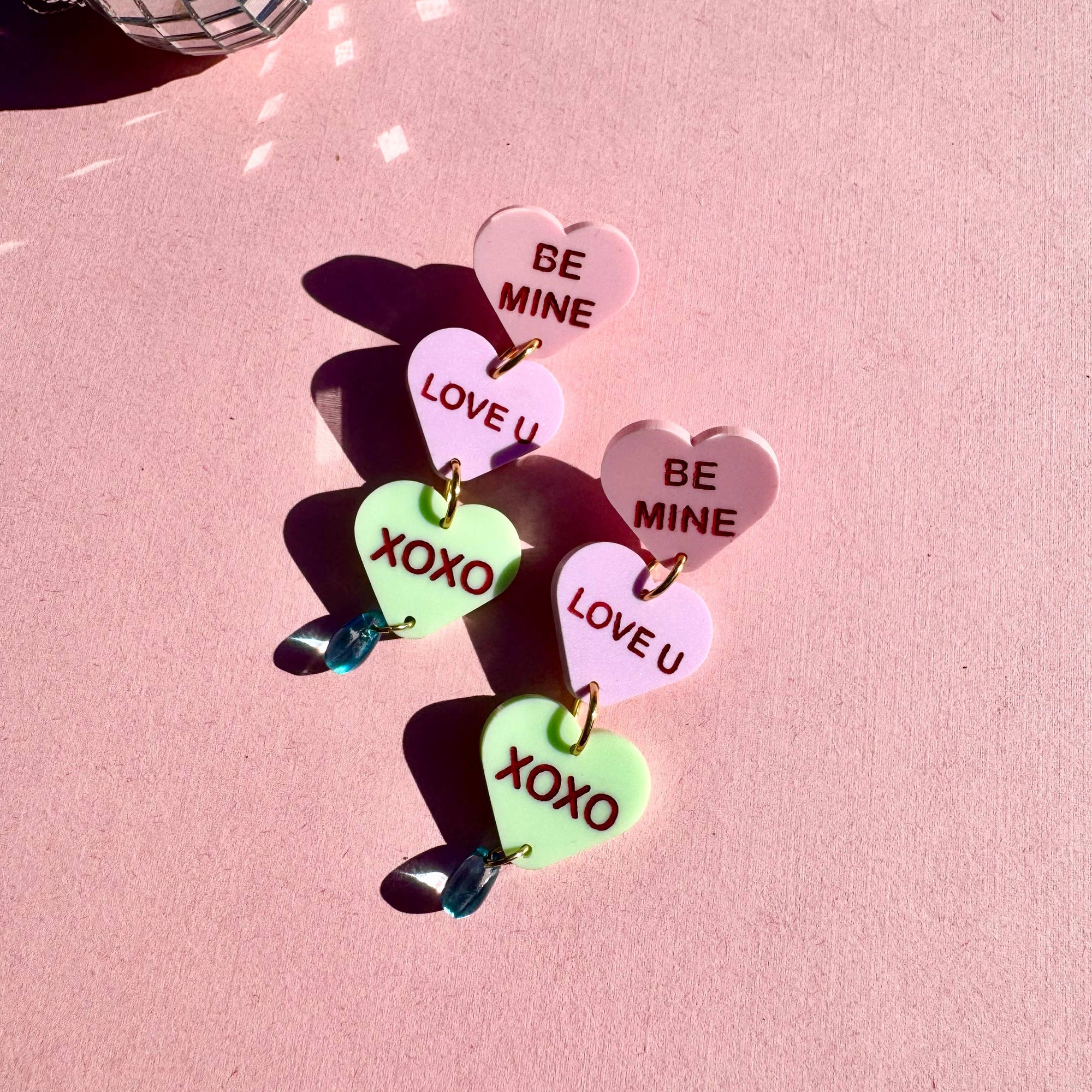 Colorful heart-shaped earrings with love messages on a pink background