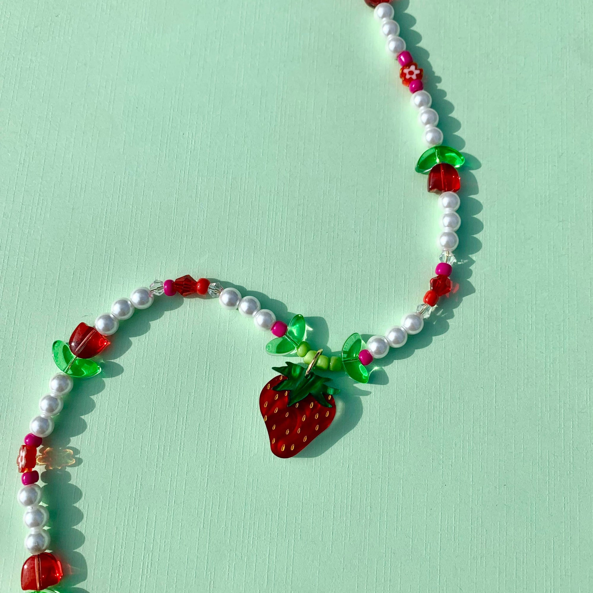 Necklace with strawberry-shaped beads on a light green background