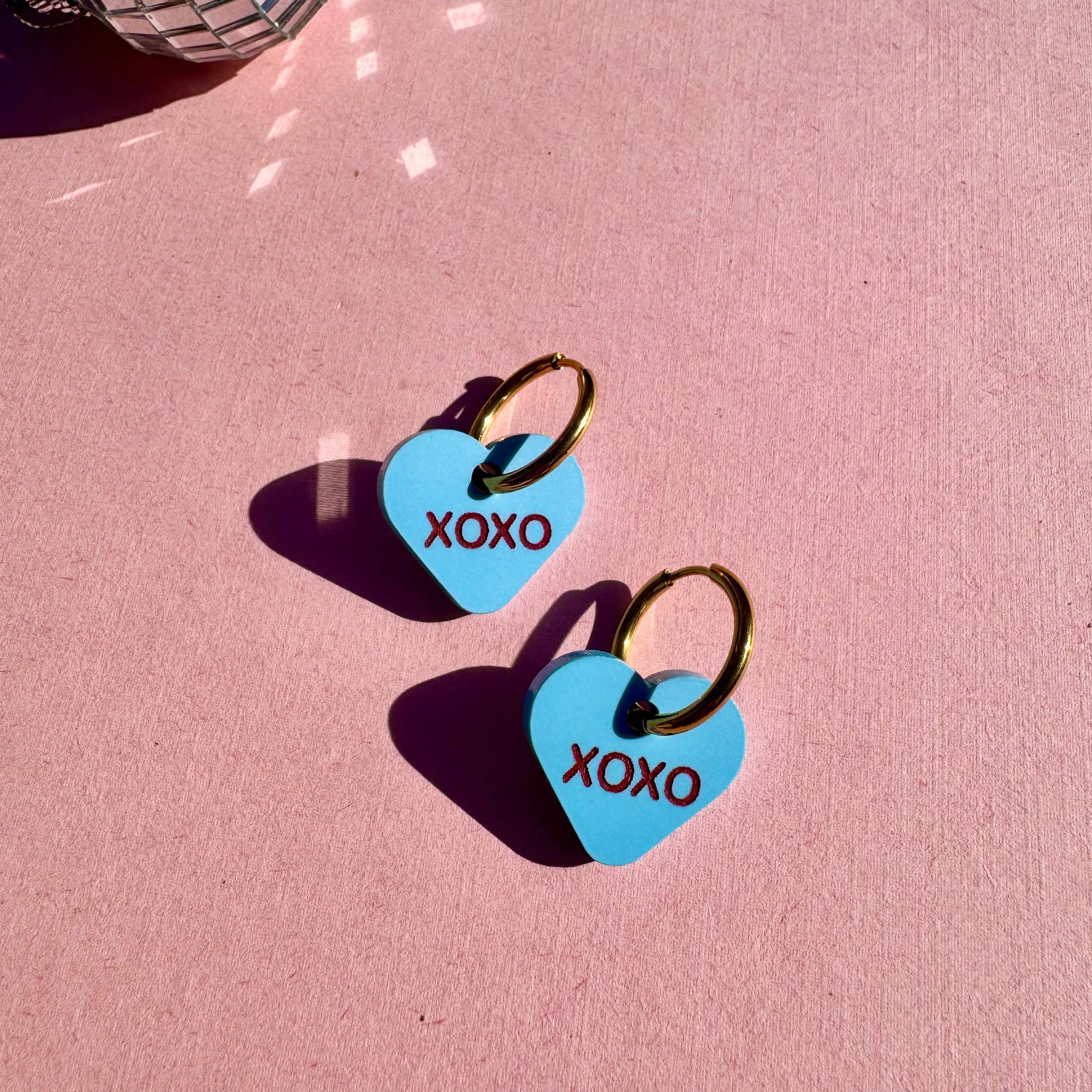 Heart-shaped earrings with 'XOXO' text on a pink background