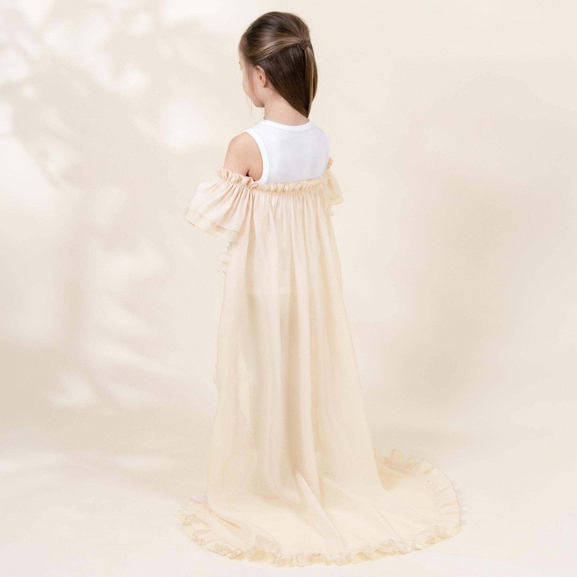 Young girl wearing a long, light-colored dress against a plain background