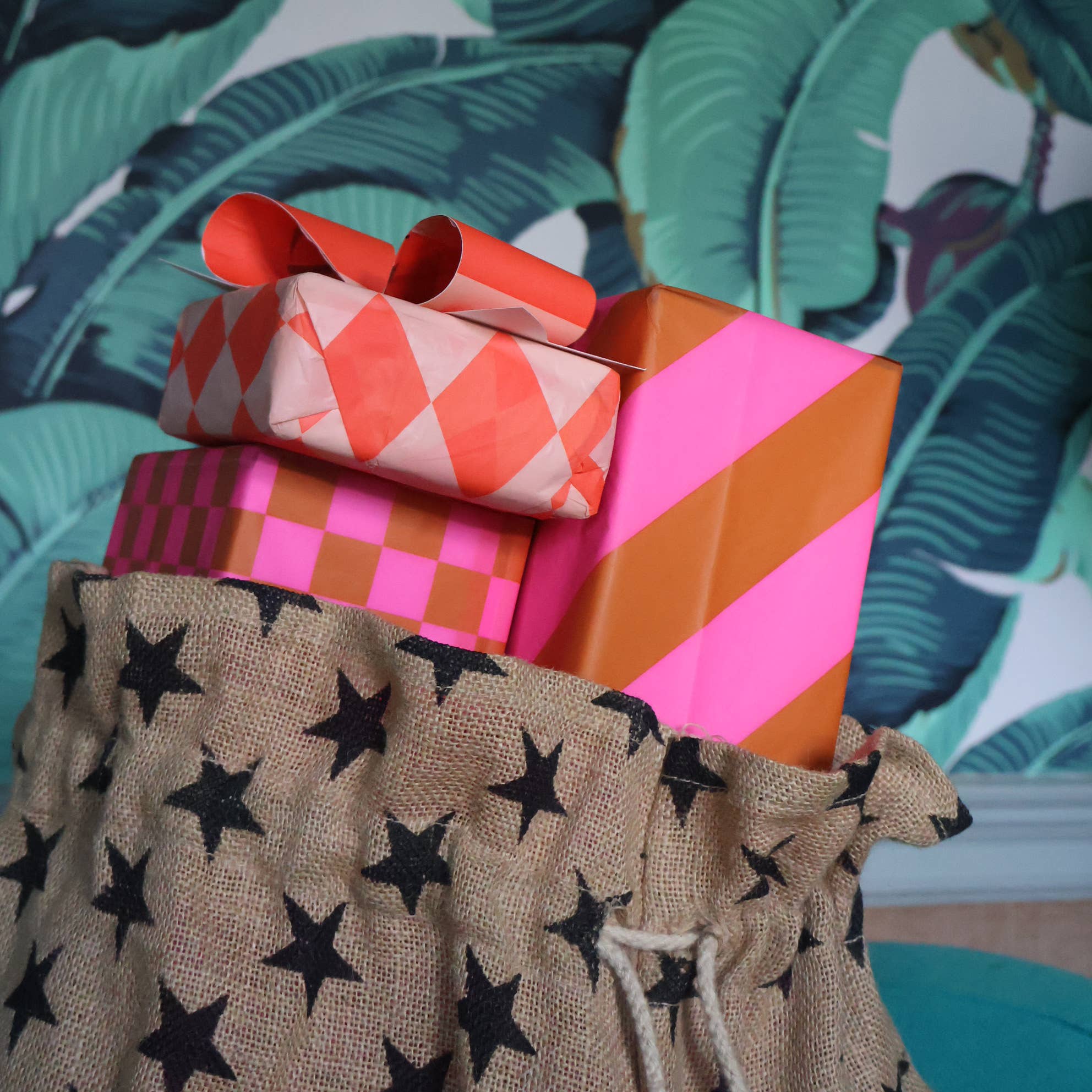 Stack of colorful wrapped presents with a star-patterned bag against a tropical leaf background