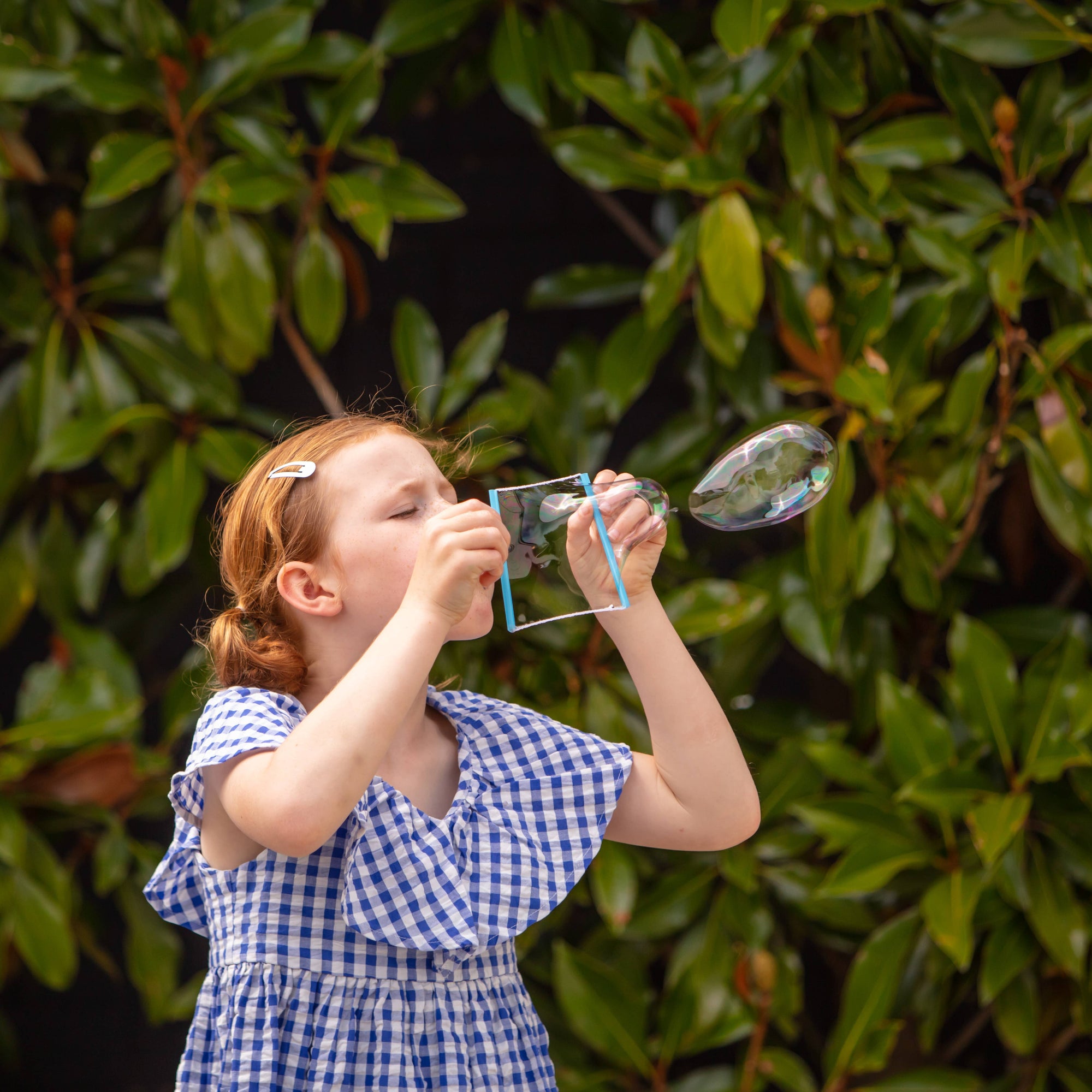 Young girl blowing bubbles against a green leafy background