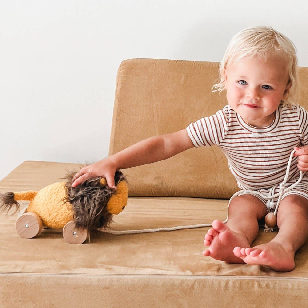 Child sitting on a beige chair with a toy lion